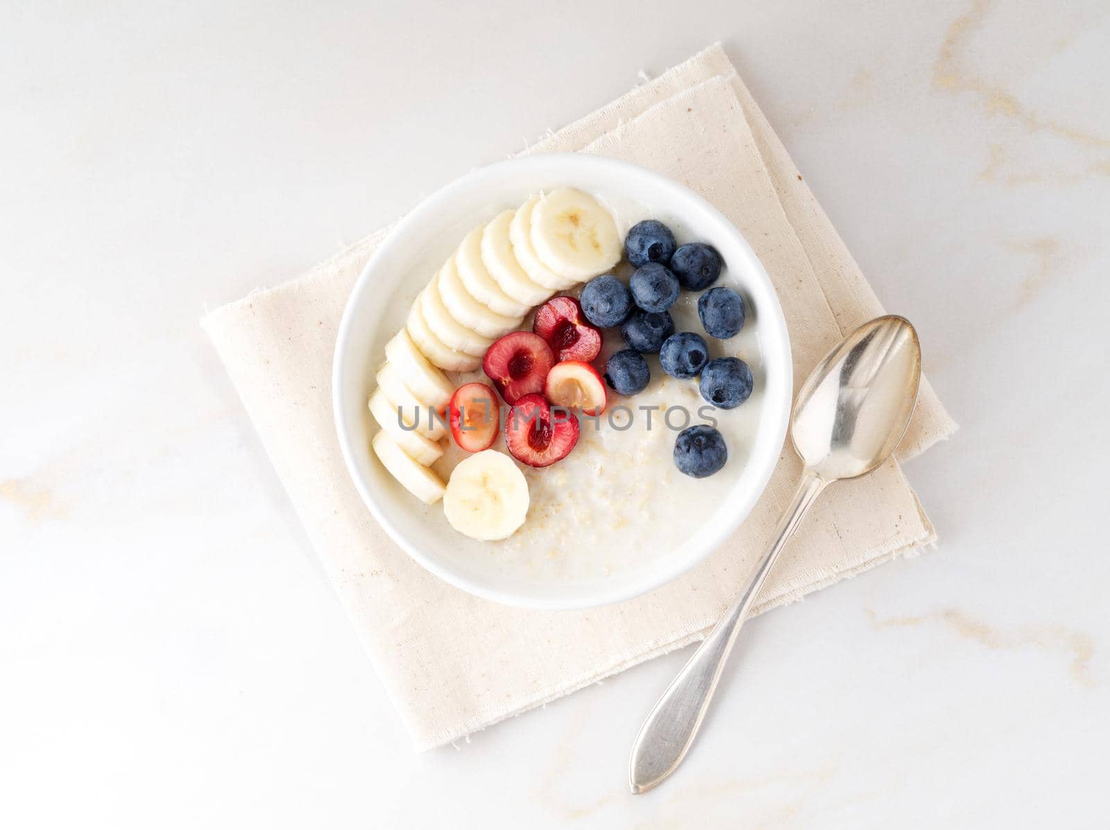 Large bowl of tasty and healthy oatmeal with a fruits and berry for Breakfast, morning meal. Top view, white marble table