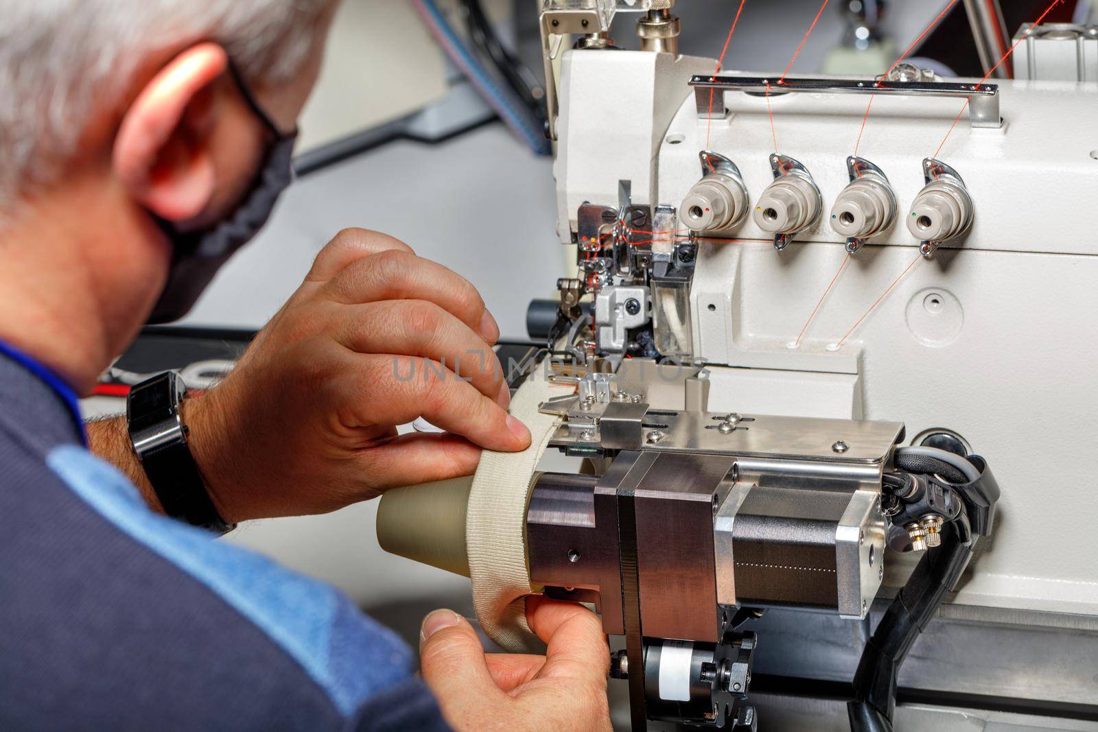 The hands of an old master set up a modern electric sewing machine and check the quality of the stitching.