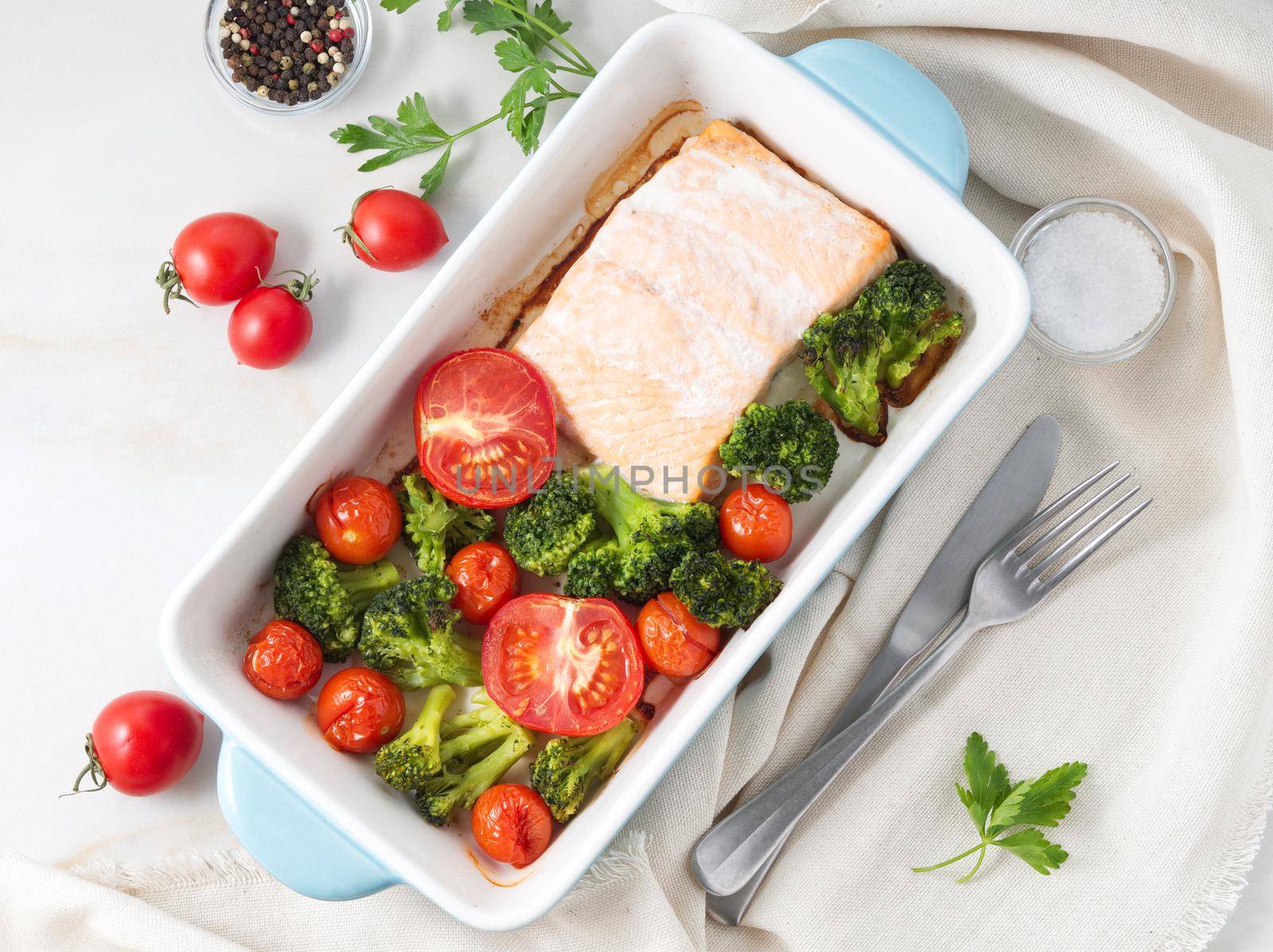 Fish salmon baked in oven with vegetables - broccoli, tomatoes. Healthy diet food, white marble backdrop, top view. by NataBene