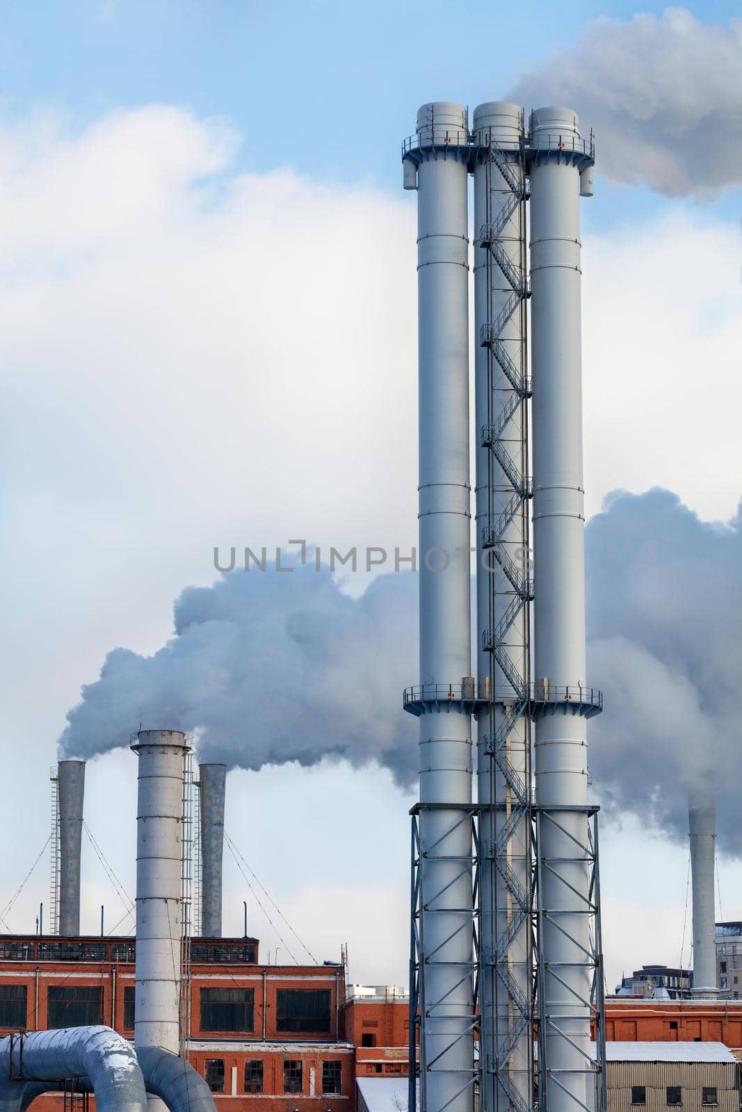 Puffs of smoke and steam rise into the sky from the city thermal station, vertical image, copy space. by Sergii