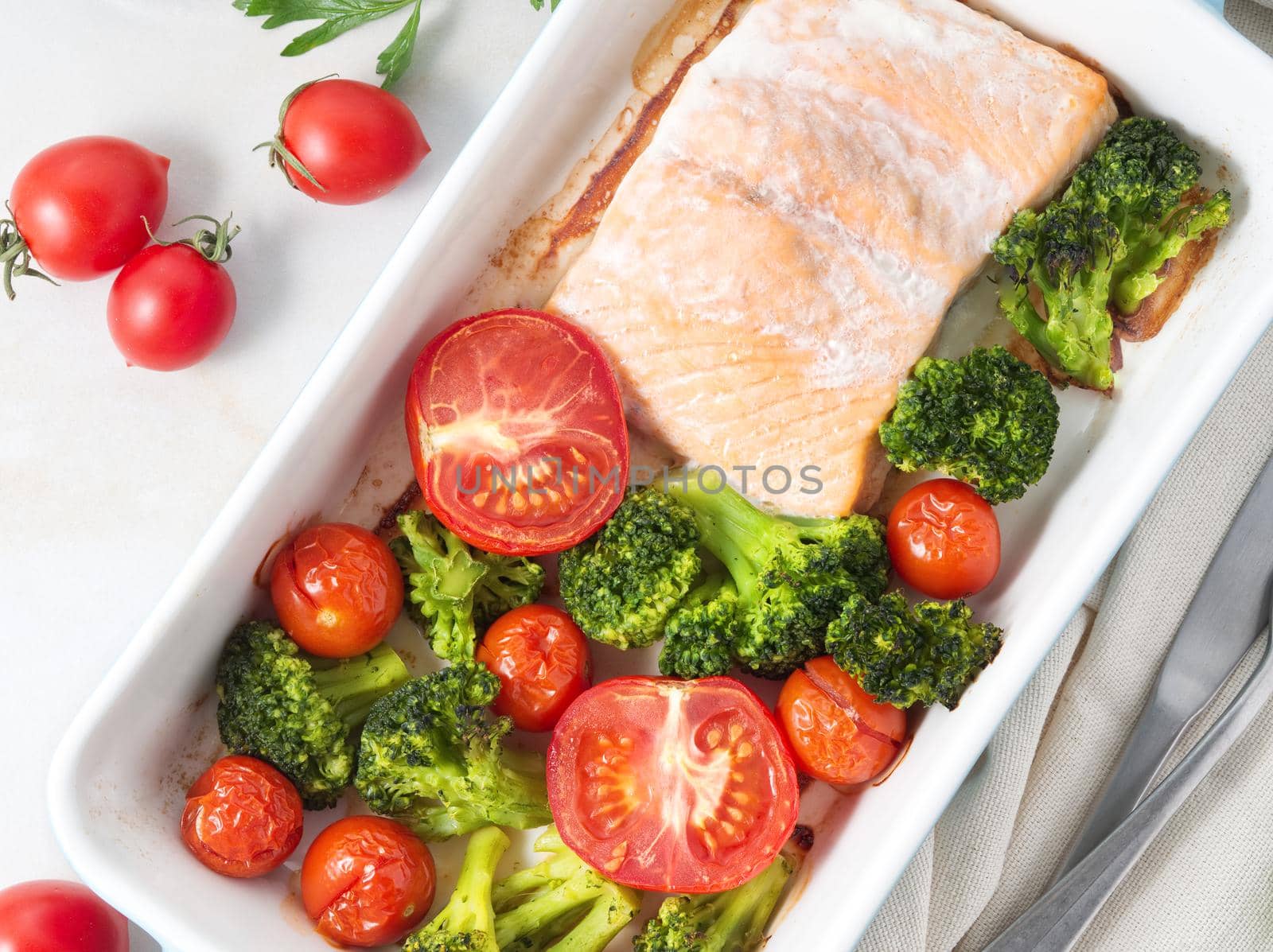 Fish salmon baked in oven with vegetables - broccoli, tomatoes. Healthy diet food, white marble backdrop, top view, close-up