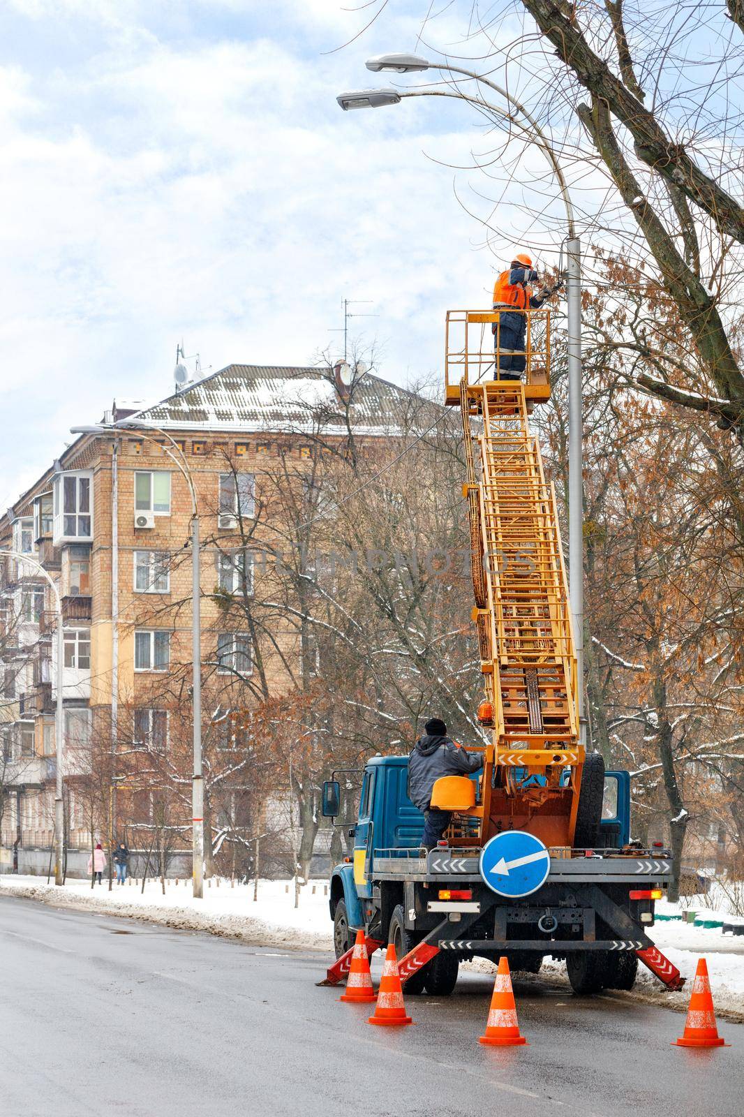 Road service workers in a truck with a telescopic ladder check the operation of street lighting in the winter. Copy space, vertical image.