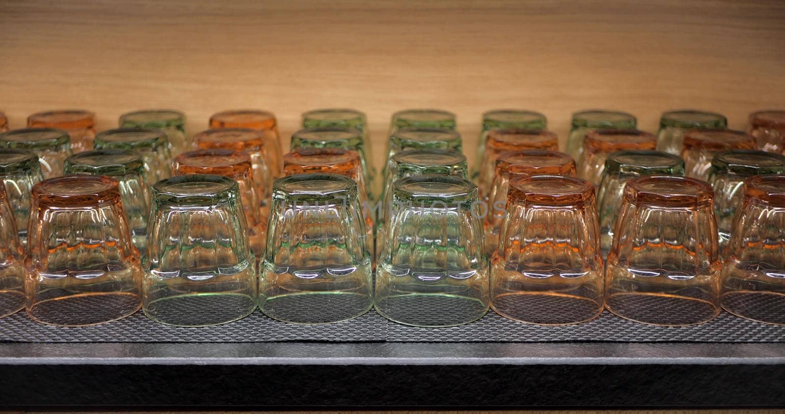 Turned drinking glasses of different colours on a shelf in a bar or restaurant. Orange and green transparent glasses for water or juice. The movement of the camera from bottom to top .