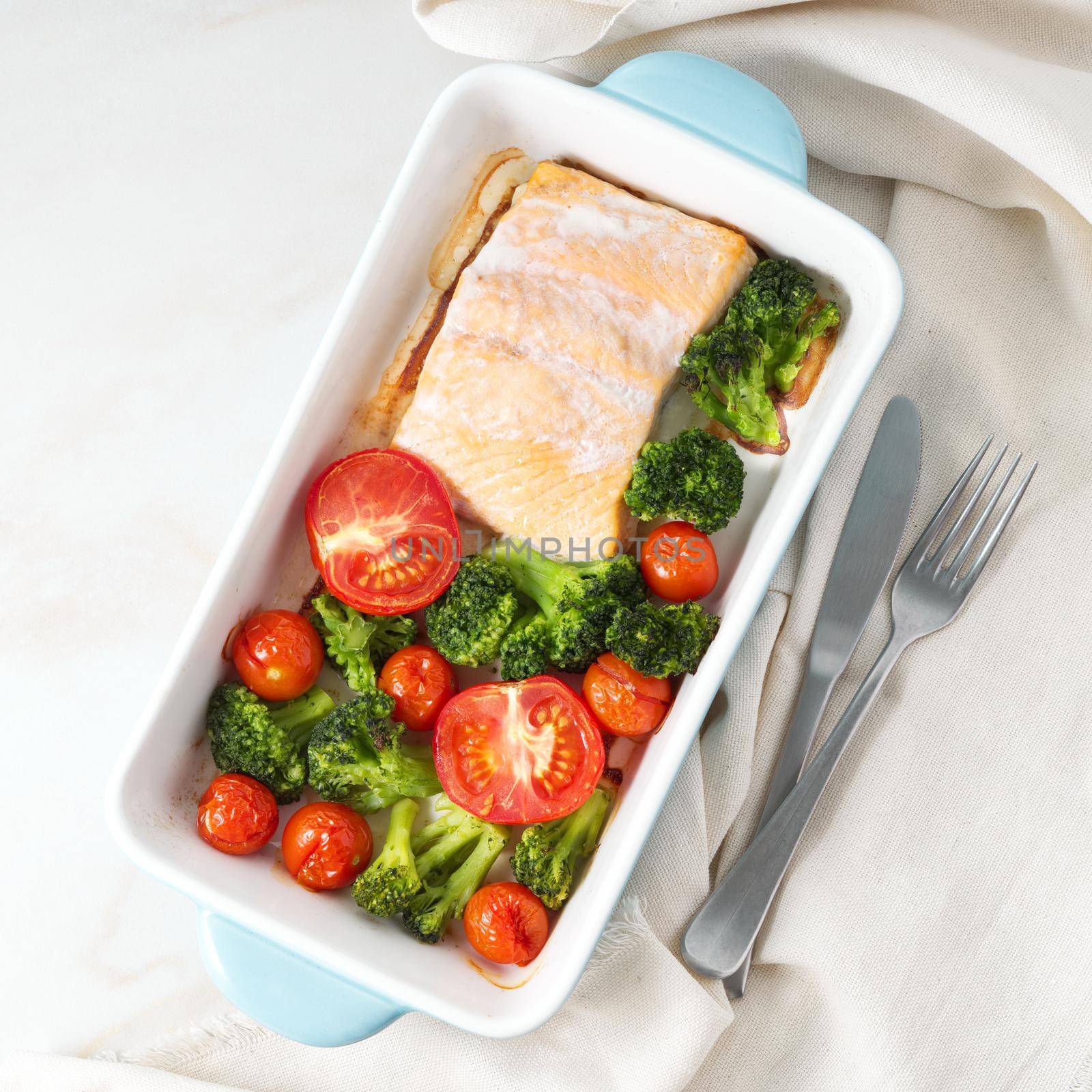 Fish salmon baked in oven with vegetables - broccoli, tomatoes. Healthy diet food, the white marble backdrop, top view.