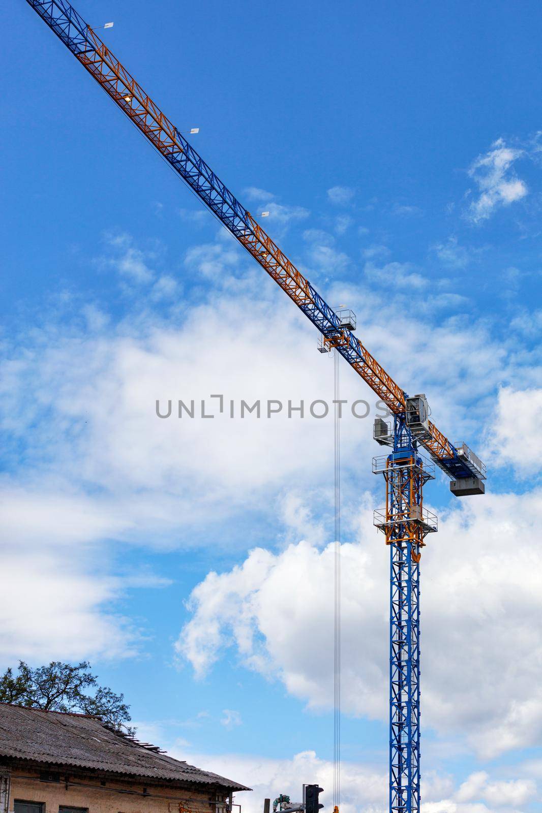 The concept of new development of residential areas of the city. An arrow of a tower crane over the roof of a dilapidated old house against the blue sky. Copy space.