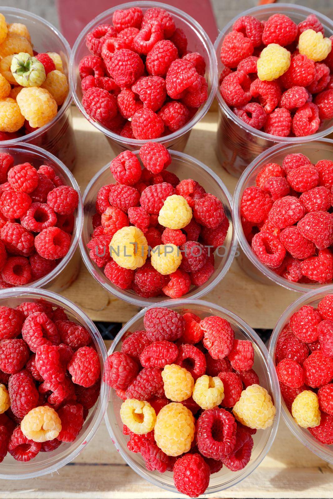 Red and yellow ripe raspberries are sold at street markets in plastic cups, top view.