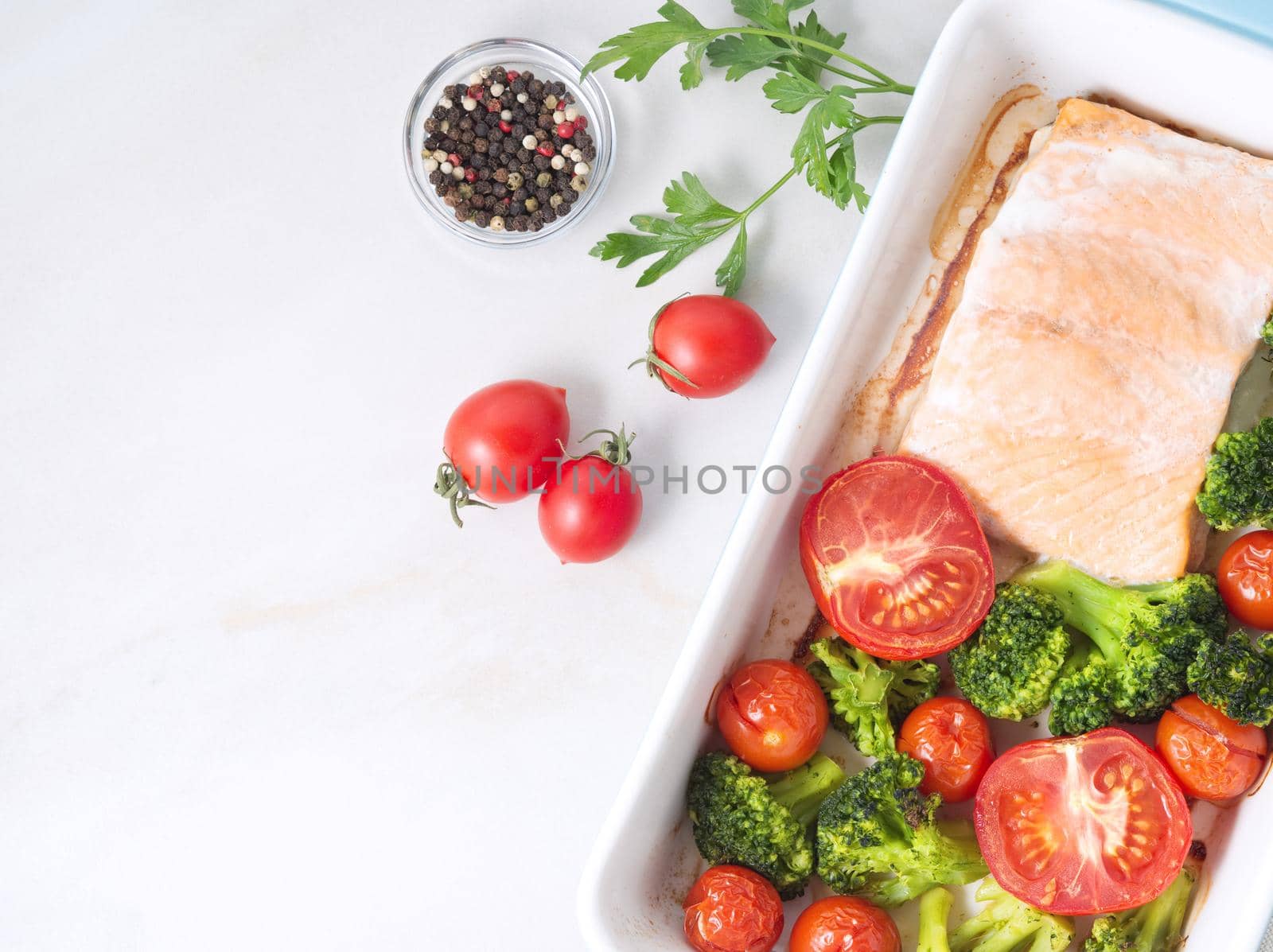 Fish salmon baked in oven with vegetables - broccoli, tomatoes. Healthy diet food, white marble backdrop, top view, close-up