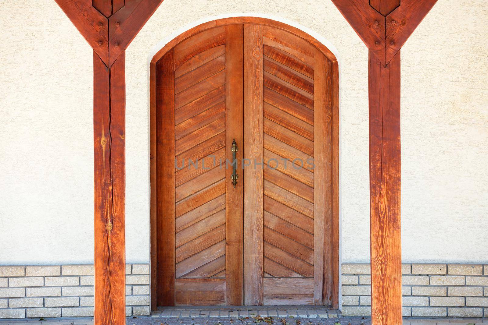 Front entrance wooden doors of a Ukrainian village hut with a massive copper handle and two symmetrical wooden supports. by Sergii