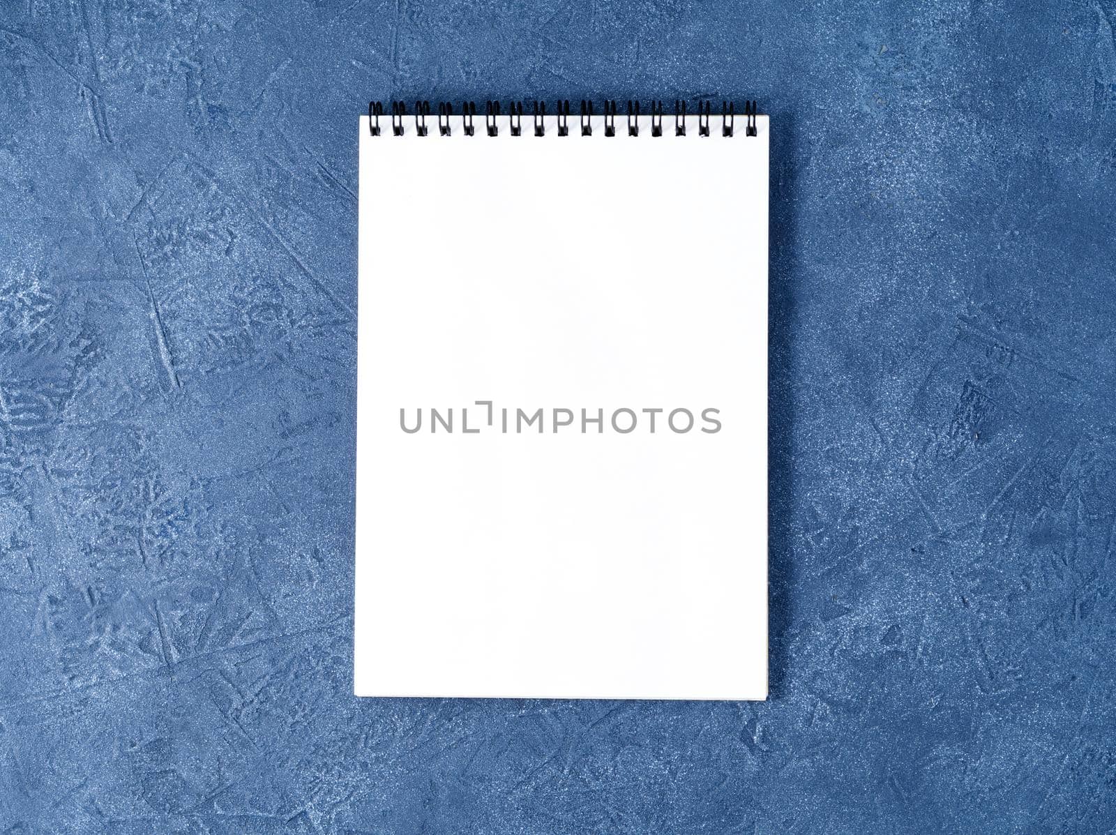 The open notepad with clean white page on a aged dark blue stone table, top view