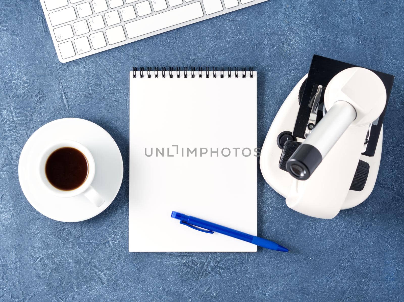 Top view of a dark blue desktop with microscope, notepad, computer. Mock up, empty space, science template