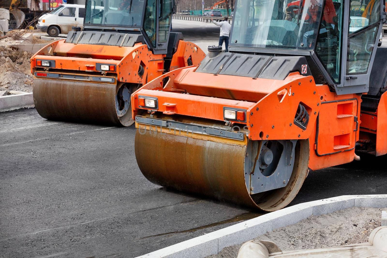 Two large vibratory road rollers compact the fresh asphalt on a new stretch of road. by Sergii