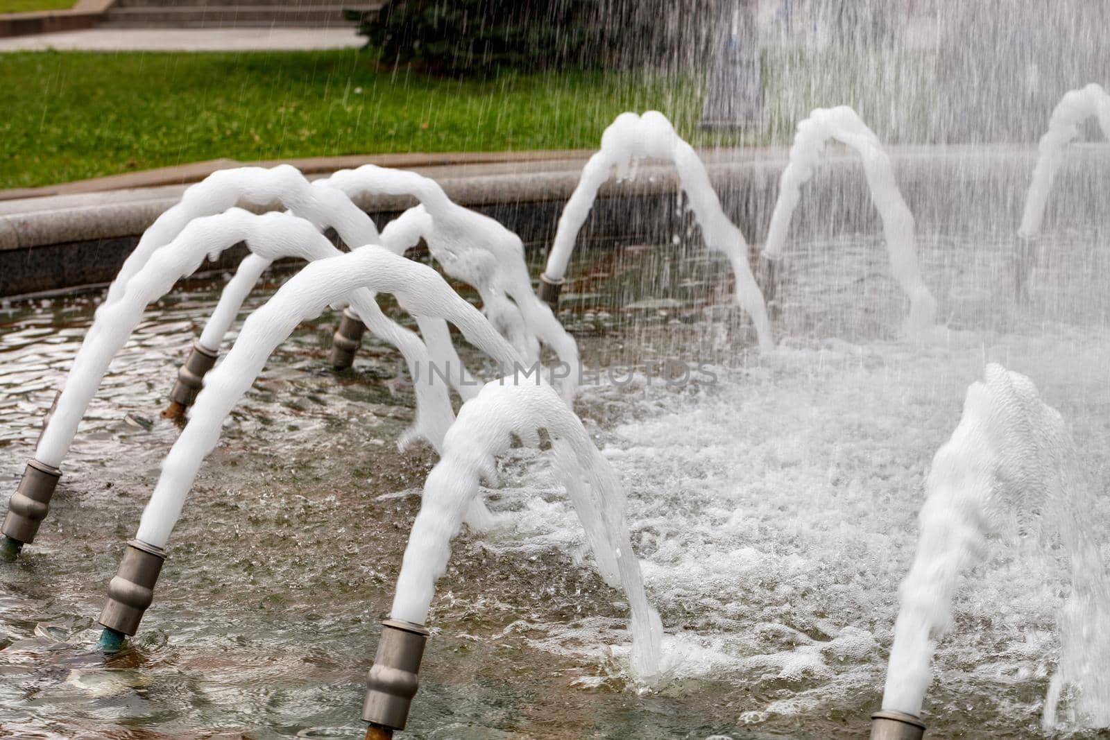 Foamed, dense jets of water burst from metal nozzles in the city fountain. by Sergii