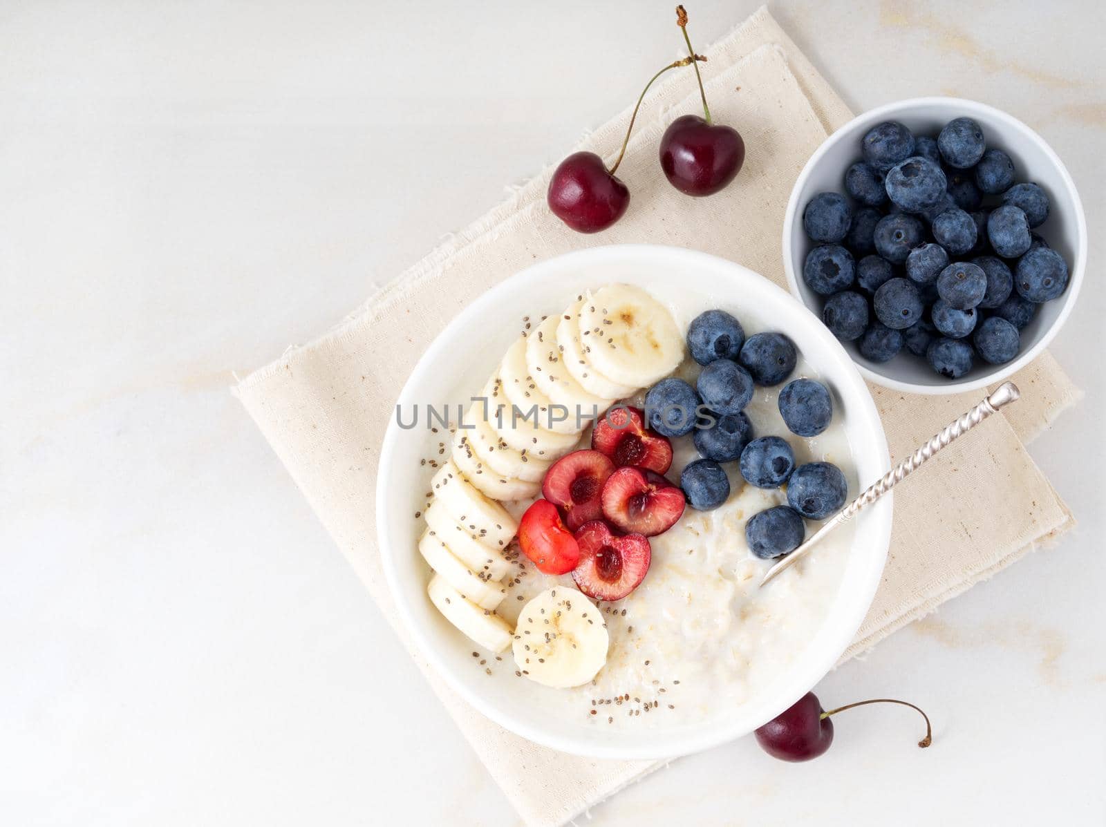 Large bowl of tasty and healthy oatmeal with fruits and berry for Breakfast, morning meal. Top view, white marble table, copy space