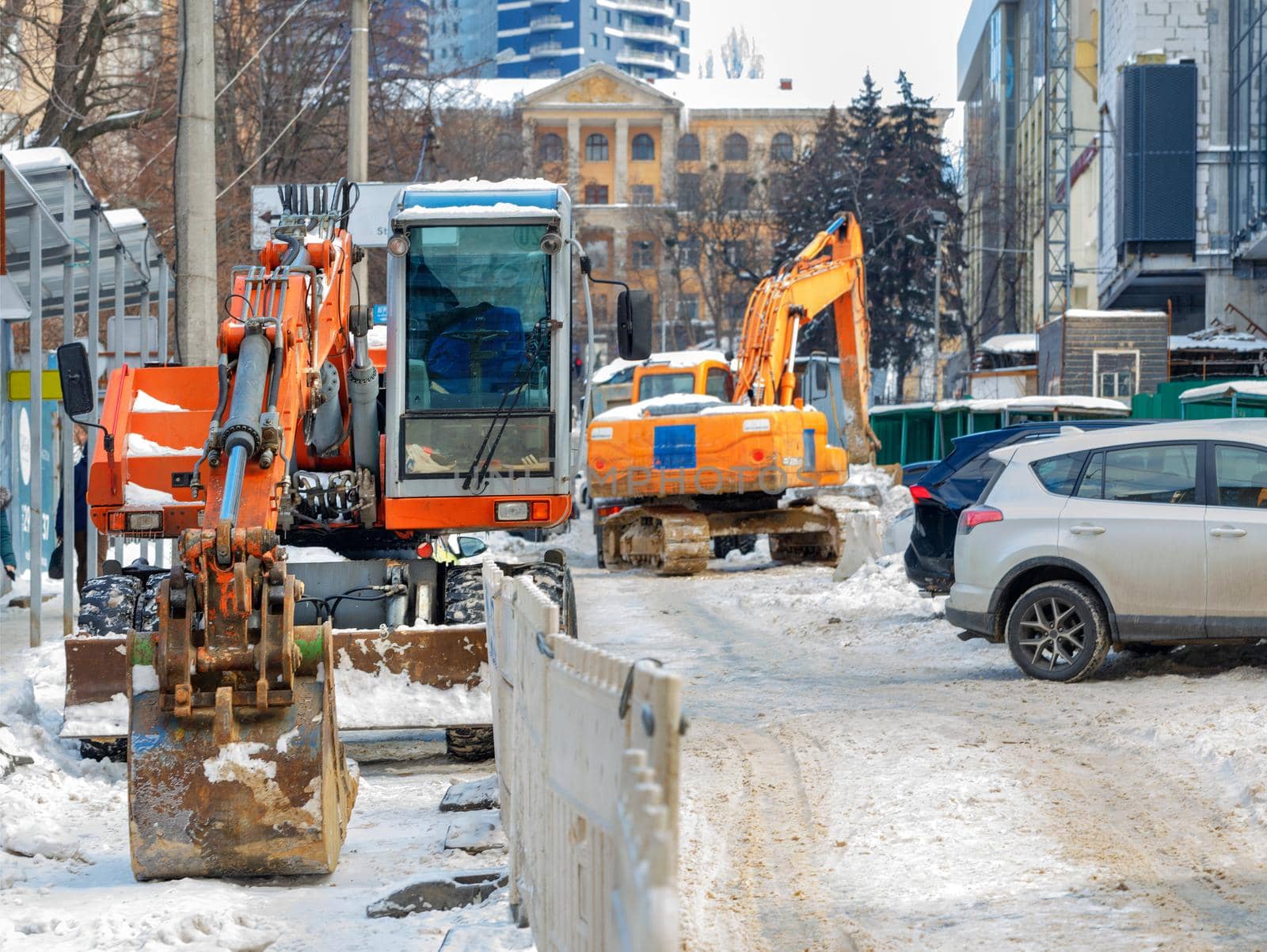 Large excavators with metal buckets clear the roadway of a city street from an abundance of snow. Selective focus.