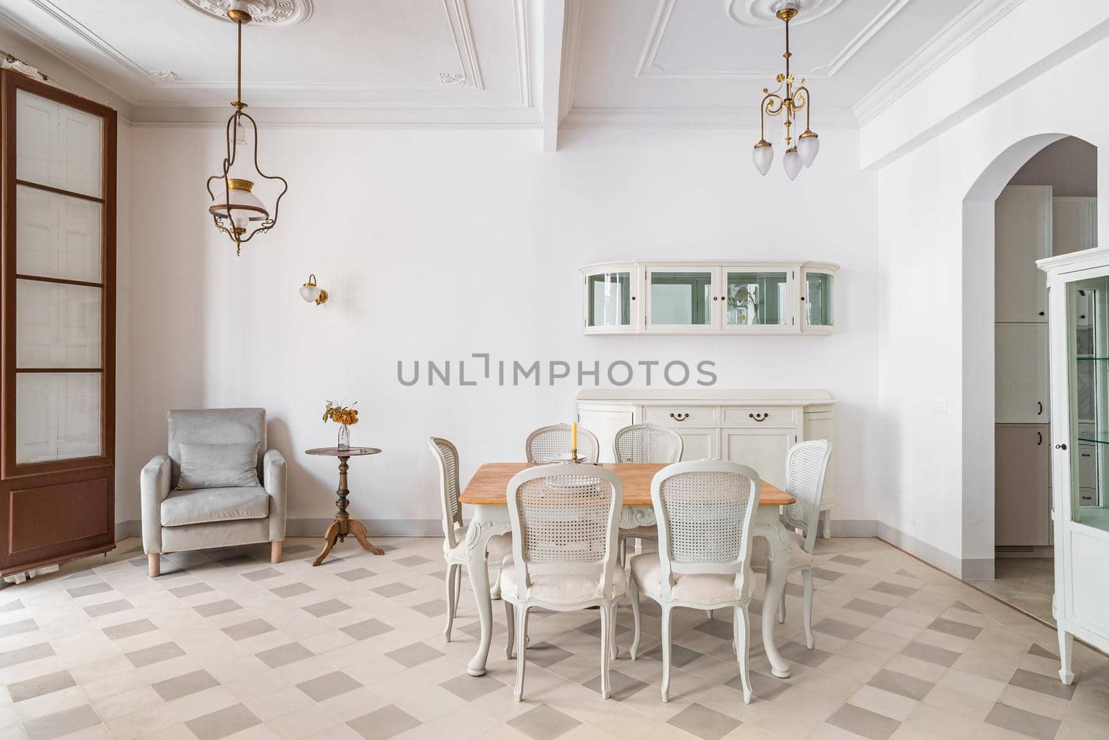 Dining table in a center of living room decorated in retro style. Tile floor and vintage chandeliers in refurbished apartment in Barcelona. Beautiful bright interior.