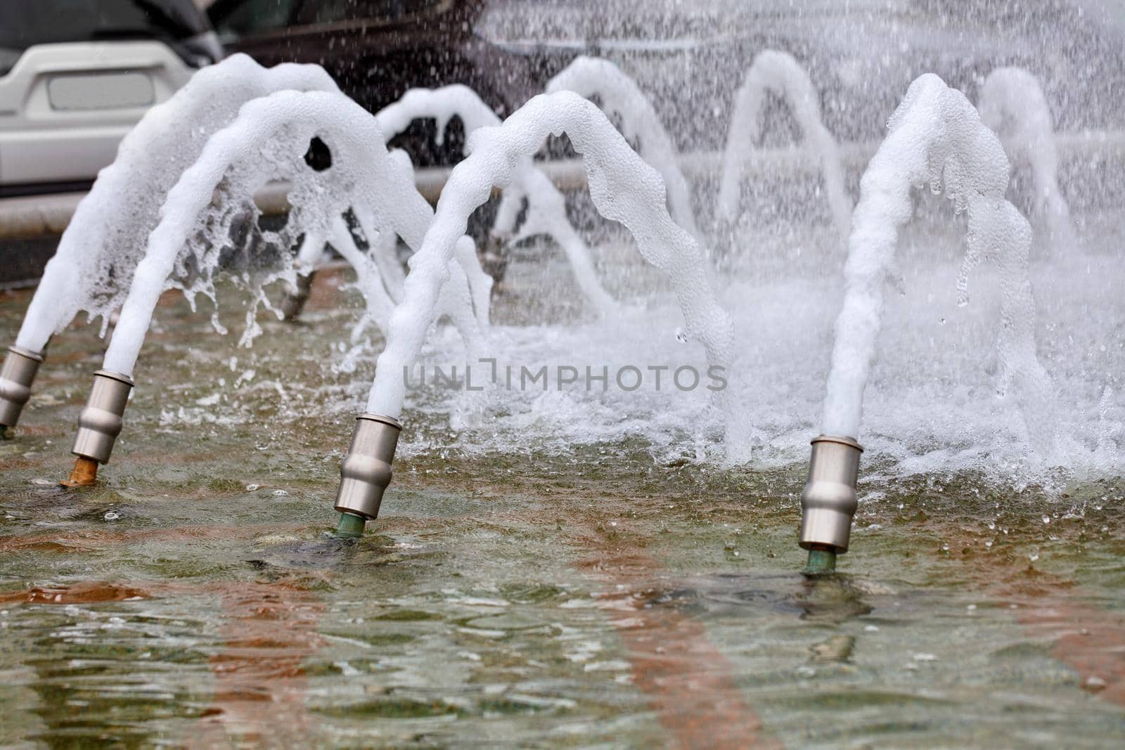Foamy dense jets of water are frozen in their motion and burst out of the metal nozzles of the city fountain. by Sergii
