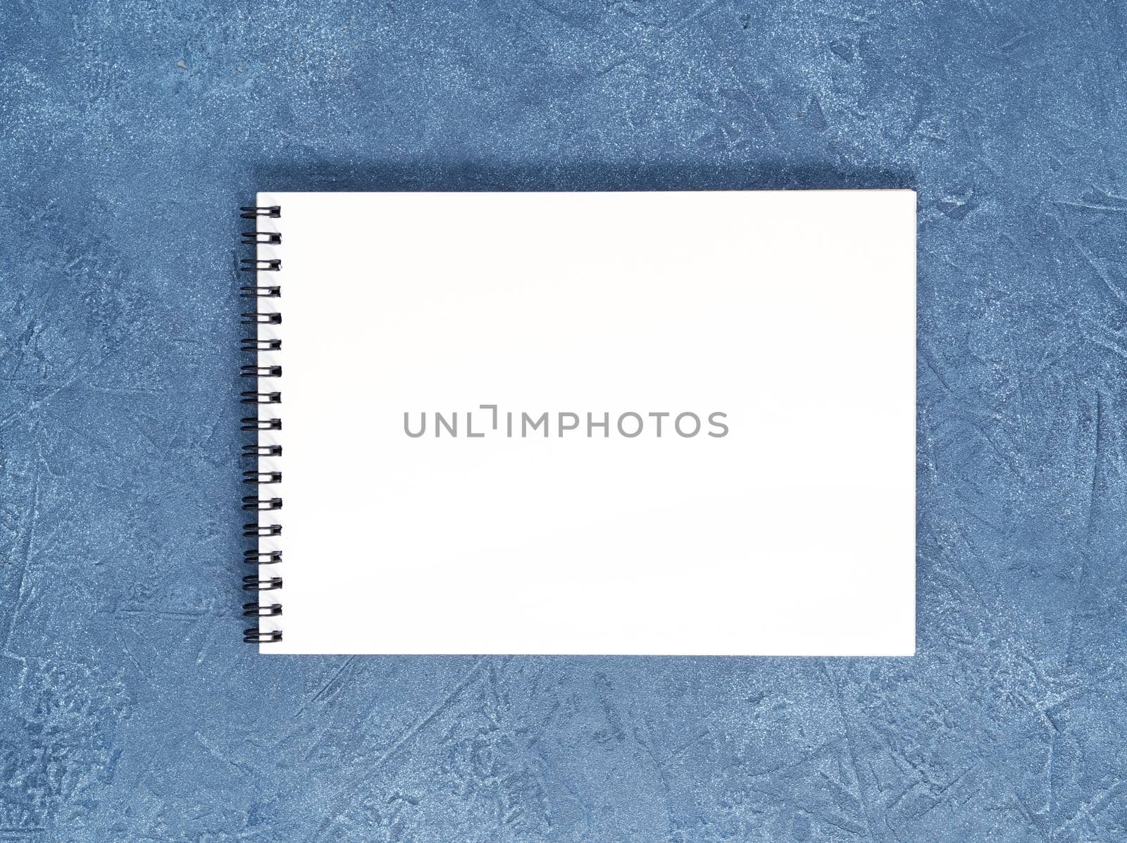 The open notepad with clean white page on a aged dark blue stone table, top view