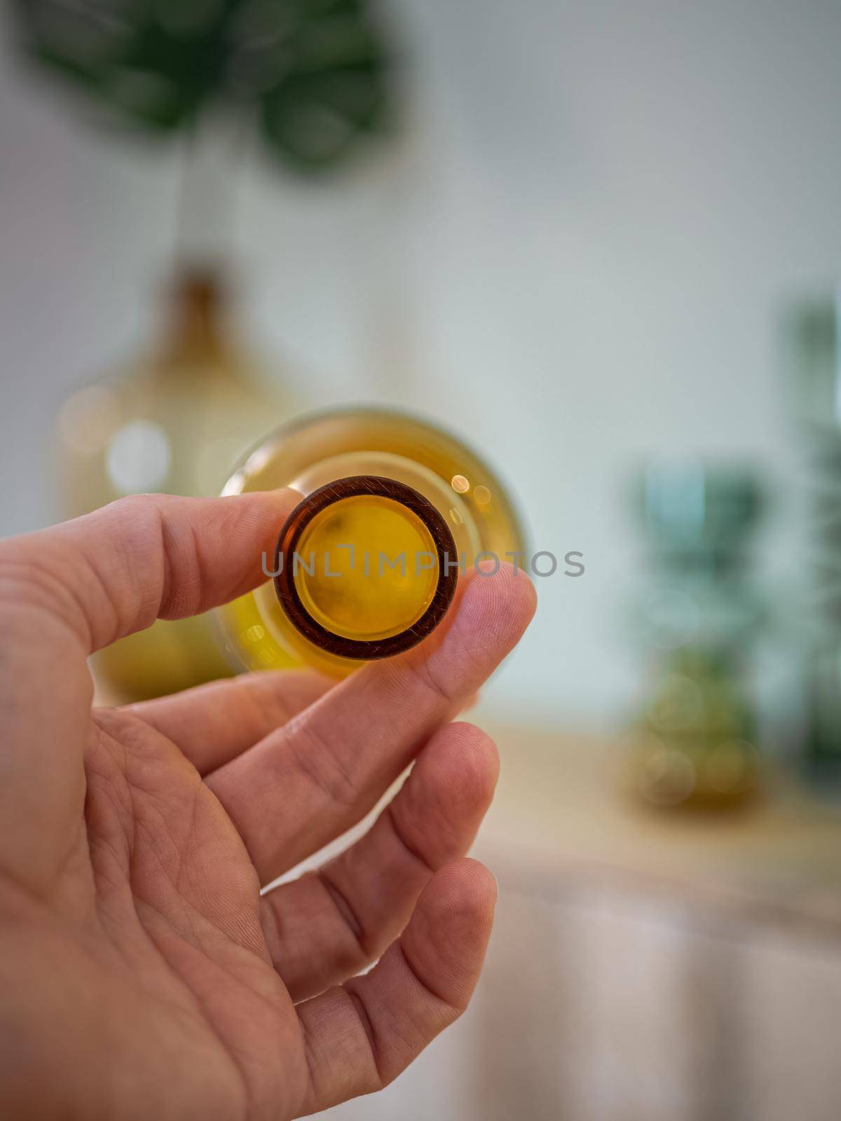 Men's hand holding a transparent yellow bottle with blurred background in interior