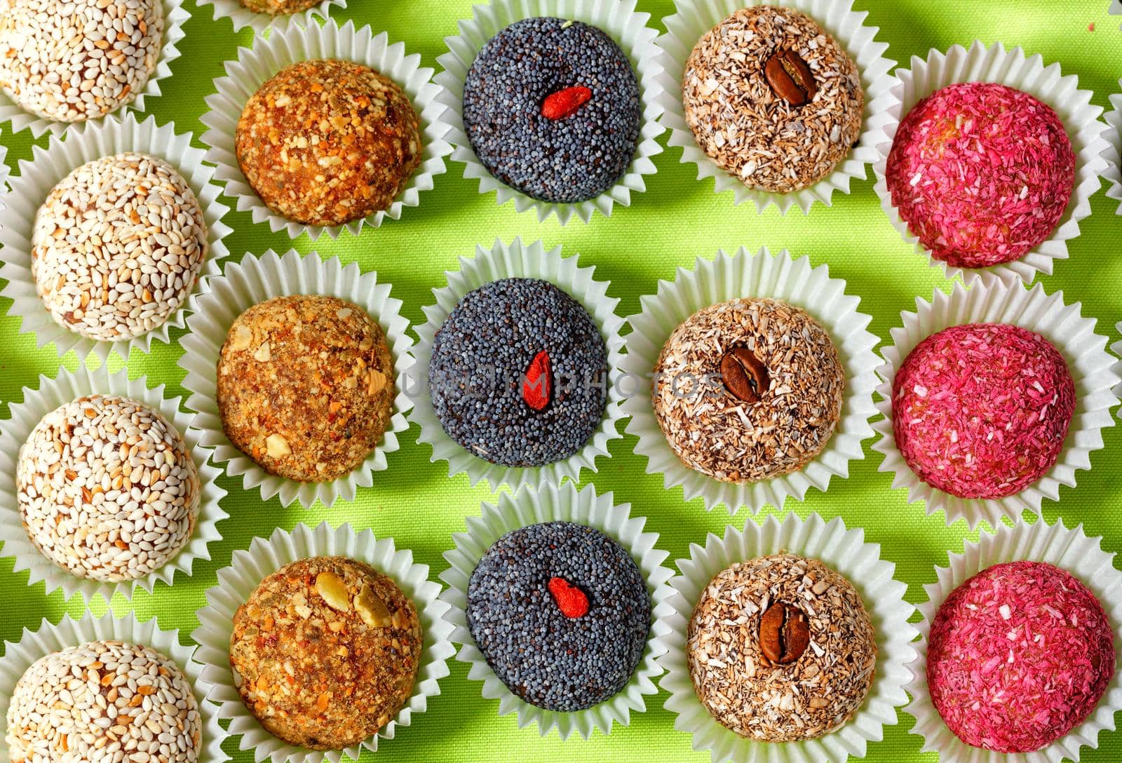 Collection of handmade energy balls with various seed fillings in paper baskets, healthy dessert and appetizer on a bright light green background.