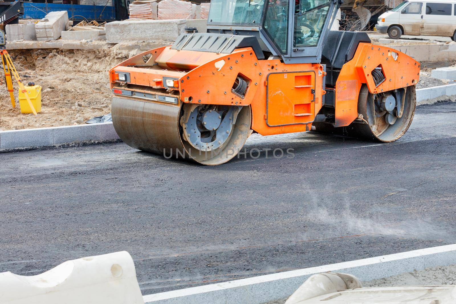 Large vibratory road roller are working on a construction site, compacting fresh asphalt. by Sergii