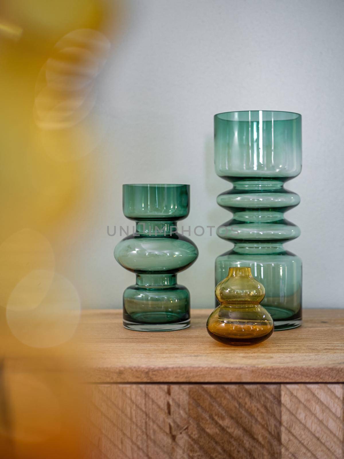 Empty decorative vases from transparent glass on wooden cupboard with blured foreground. Interior decoration.