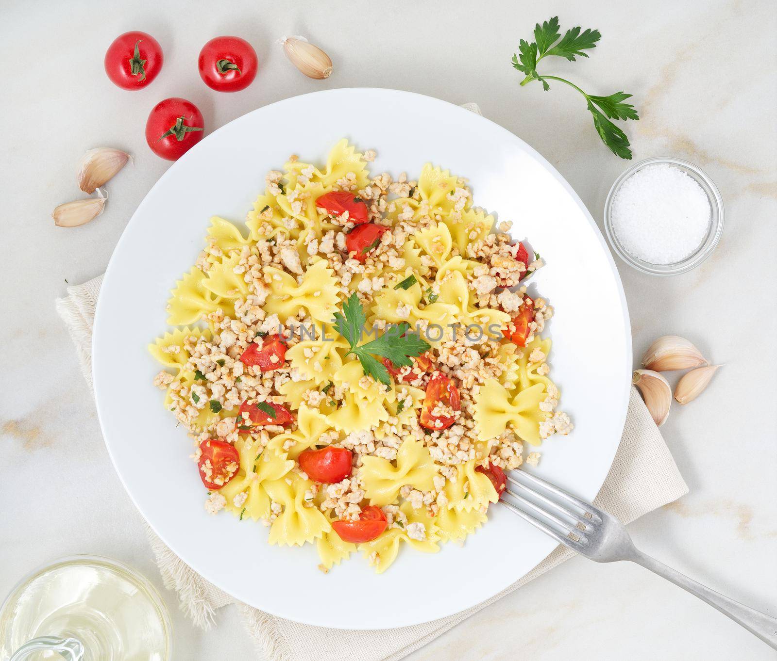farfalle pasta with tomatoes, chiken meat, parsley on white stone background, low-calorie diet, the top view
