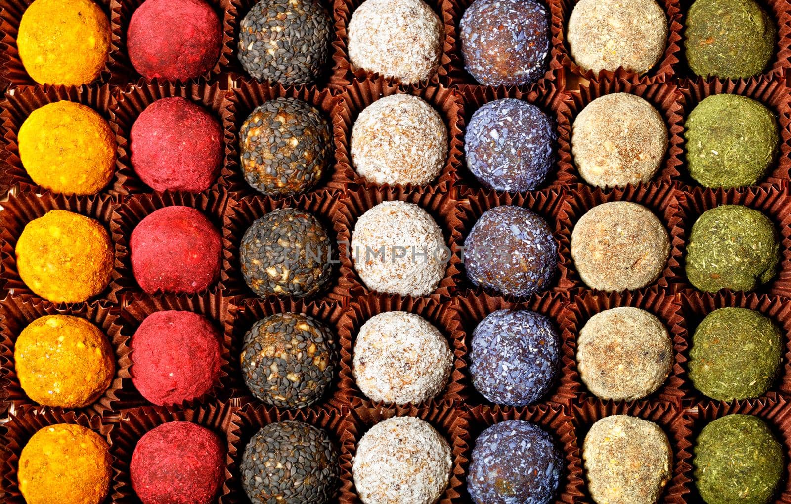 Collection of handmade energy balls with various fillings in brown paper baskets, top view. Healthy dessert and appetizer on a bright light green background.