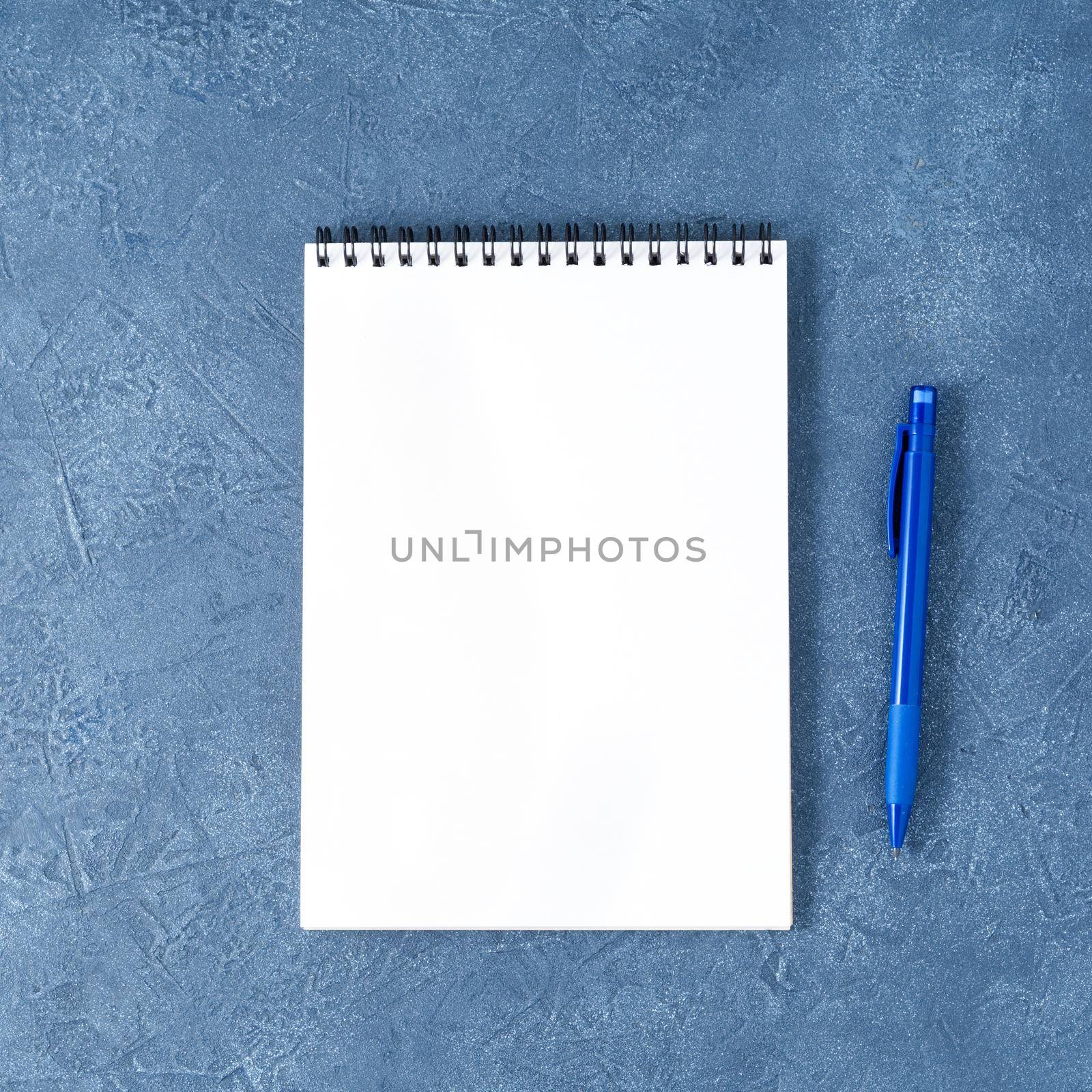 The open notepad with clean white page on aged dark blue stone table, top view by NataBene