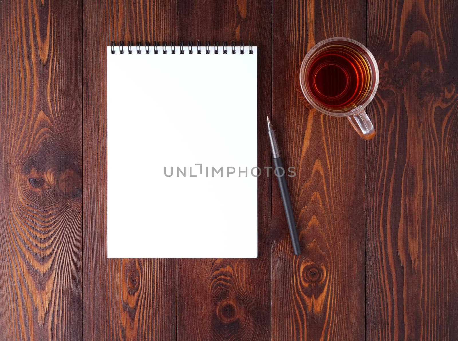 The open notepad with spiral , pencil, cup of tea on dark brown wooden table, top view by NataBene
