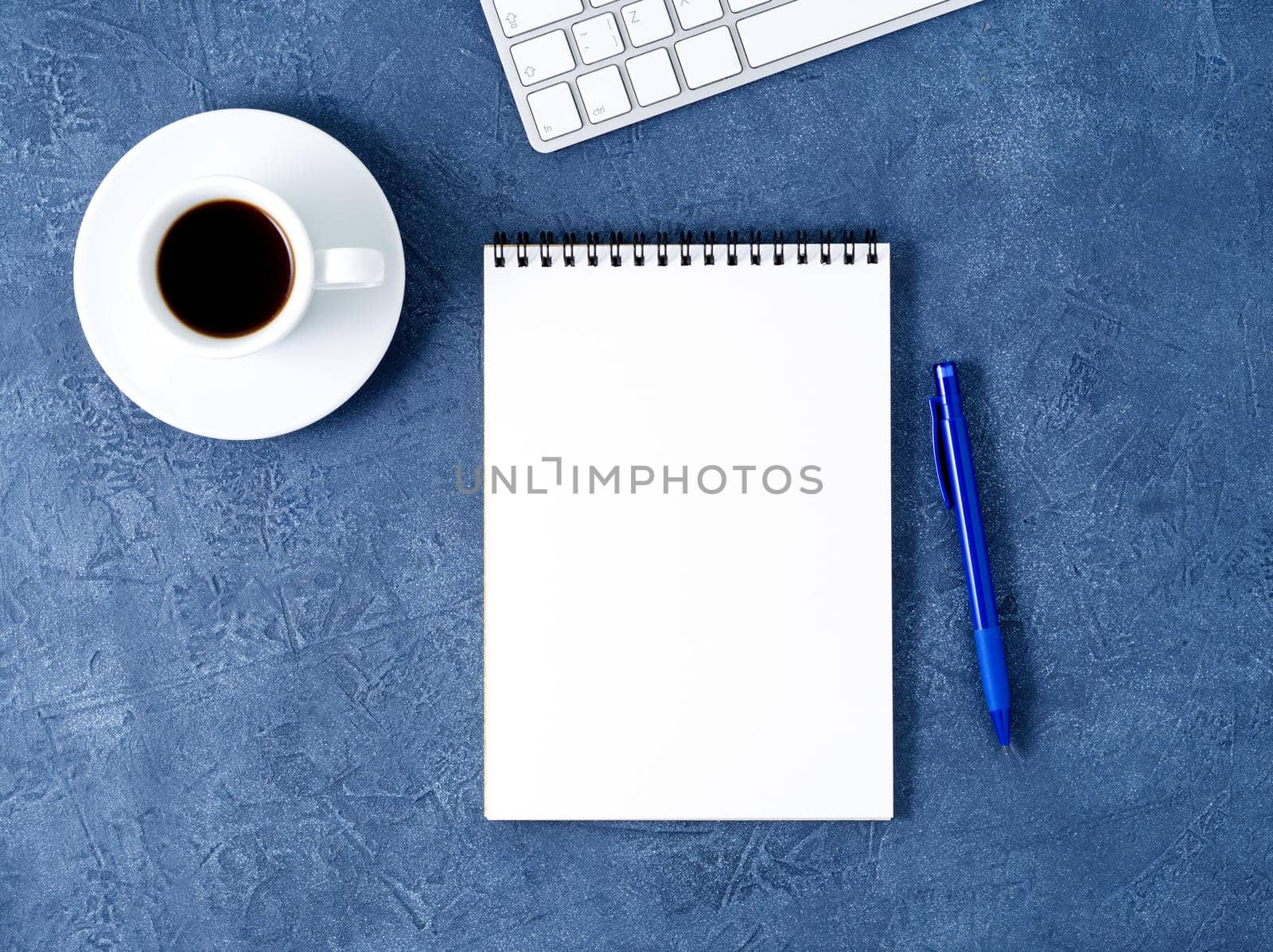 The open notepad with clean white page, pen and coffee cup on a aged dark blue stone table, top view