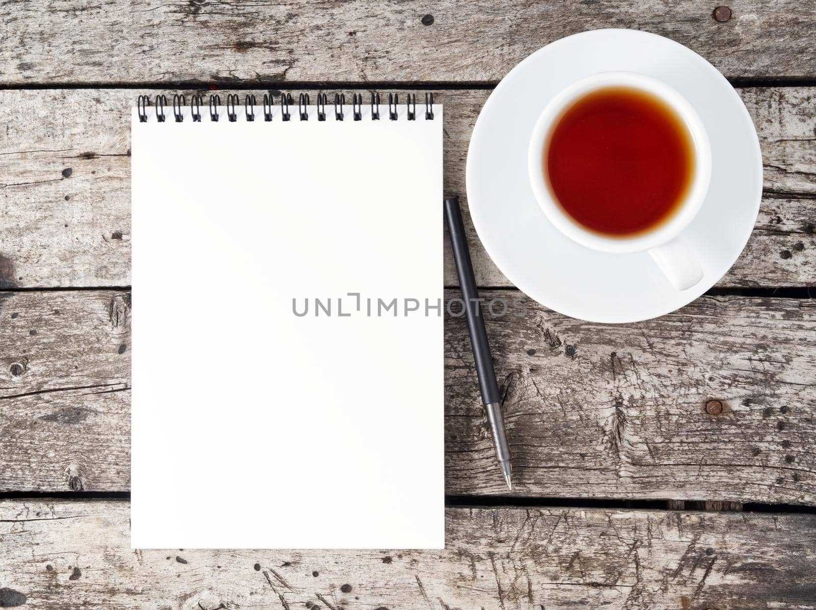 The open notepad with clean white page, pen and coffee cup on aged old rustic wooden table, top view