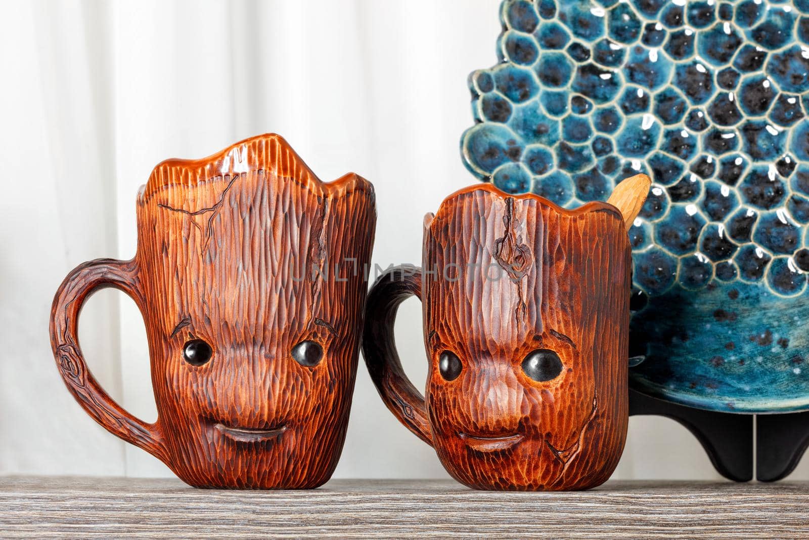 Two funny wood-styled clay cups stand on a gray wooden shelf. by Sergii