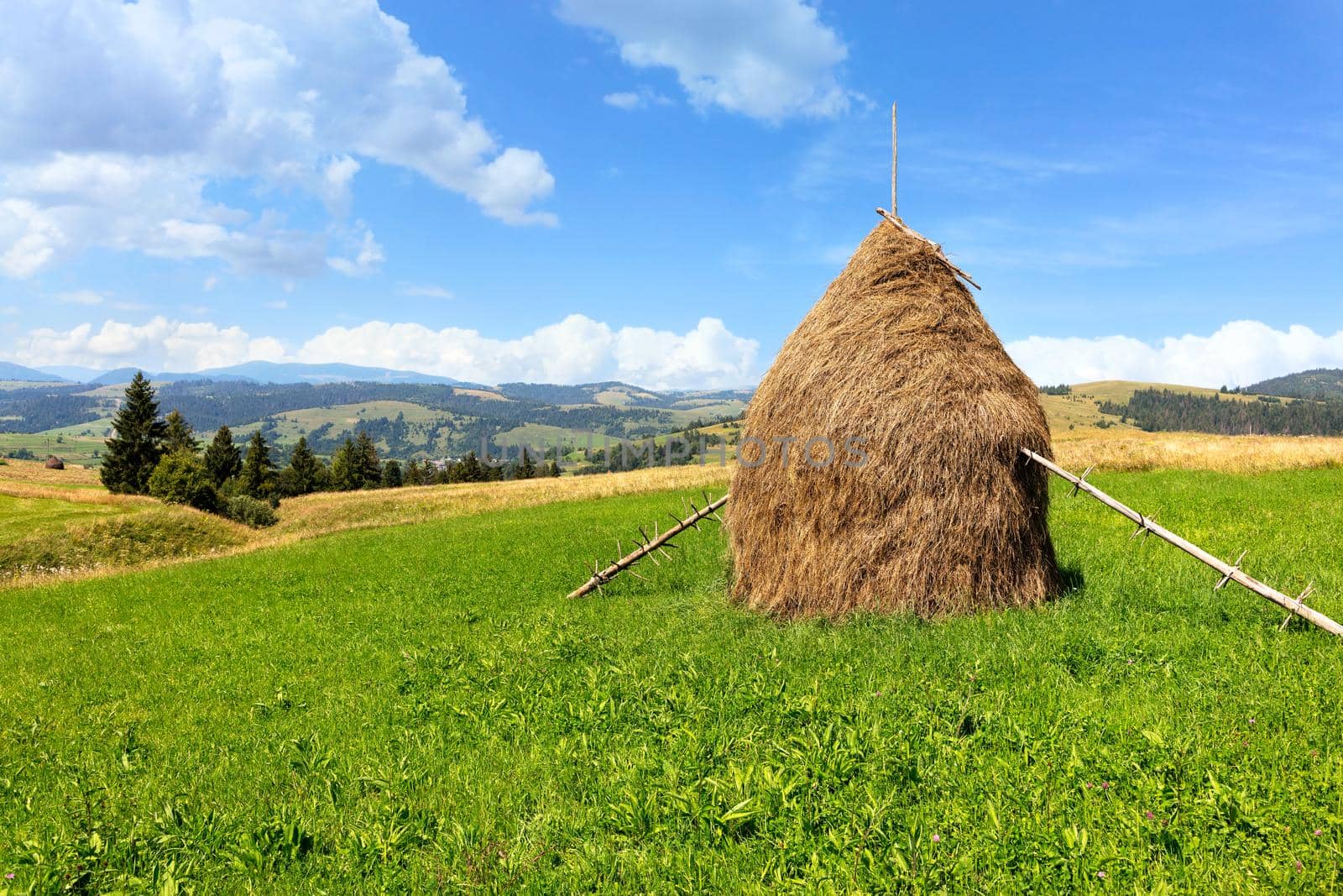 A haystack stands on a green mountain meadow against the backdrop of a beautiful summer mountainous landscape on a bright sunny day.