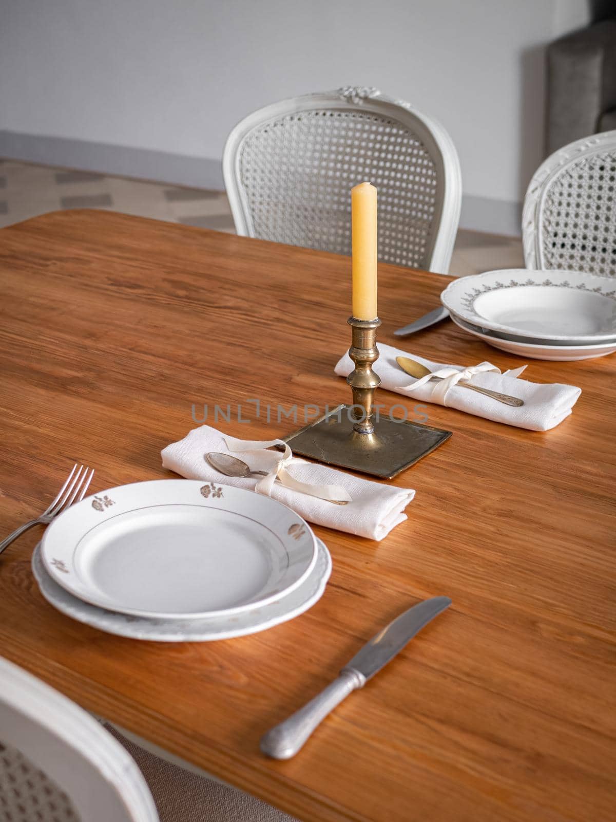 Wooden table setting for two persons, with plates, cutlery and old candlestick with candle. Interior of living room decorated in vintage style. Selective focus.