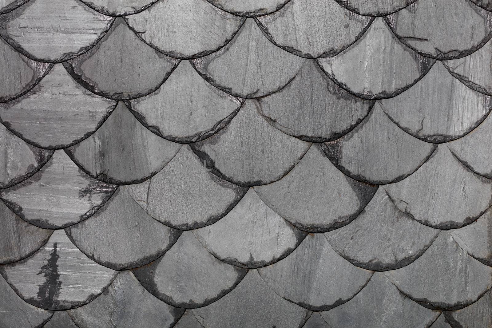 The roof is made of gray slate slabs in the shape of fish scales. Background and texture, close-up.