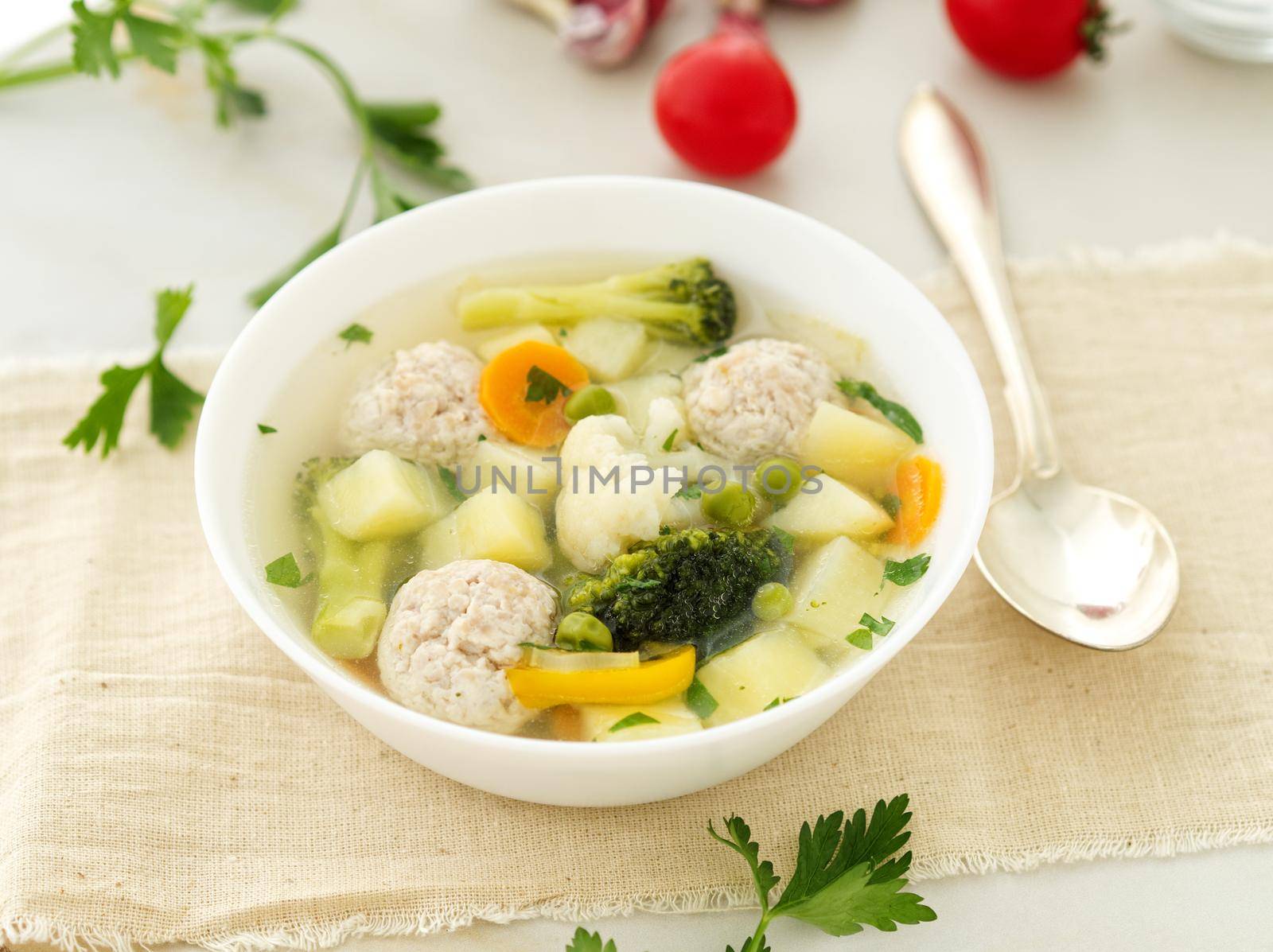 bowl of soup, a cup of broth and vegetables, meatballs made of turkey and a chicken, side view