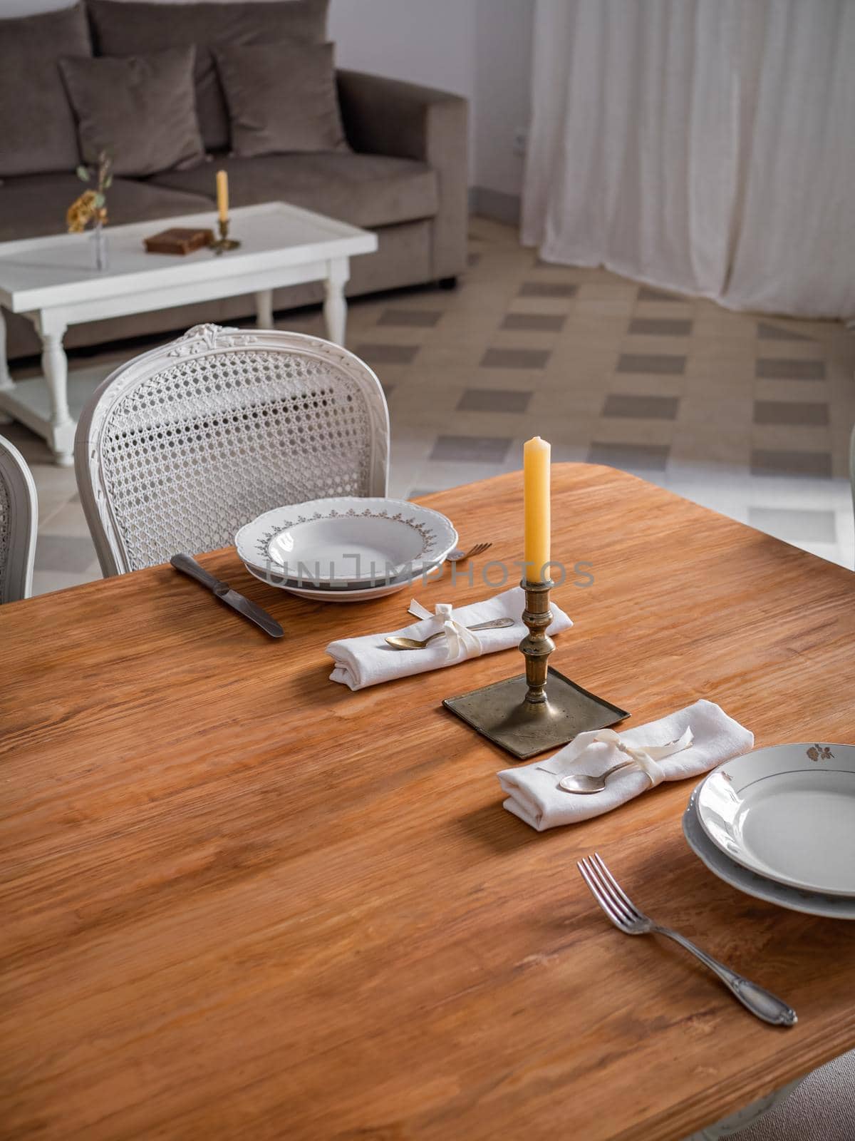 Wooden table setting for two persons, with plates, cutlery and old candlestick with candle. Interior of living room decorated in vintage style