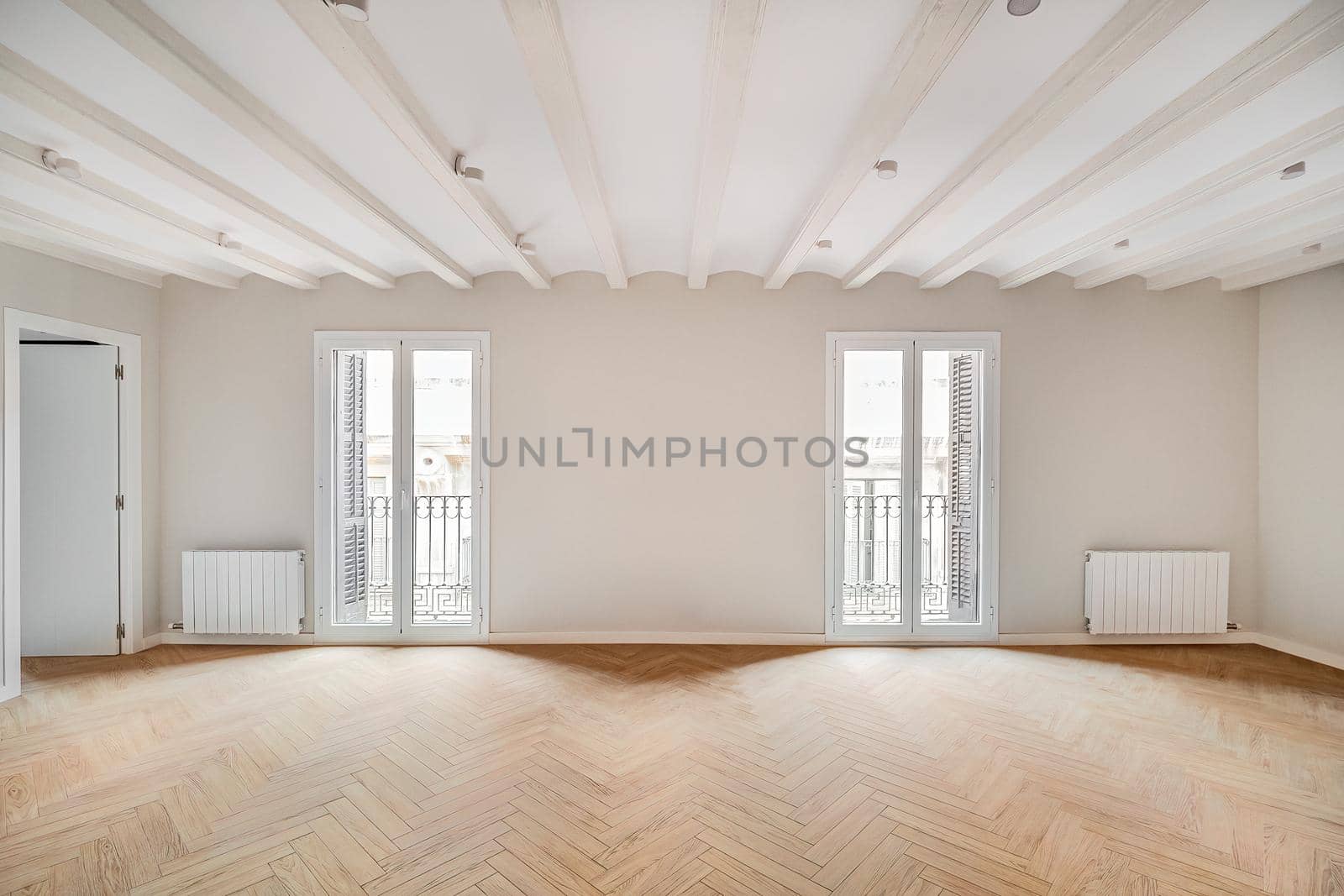 Empty and clean room in a refurbished apartment with wooden floor and two balconies. Bright real estate interior