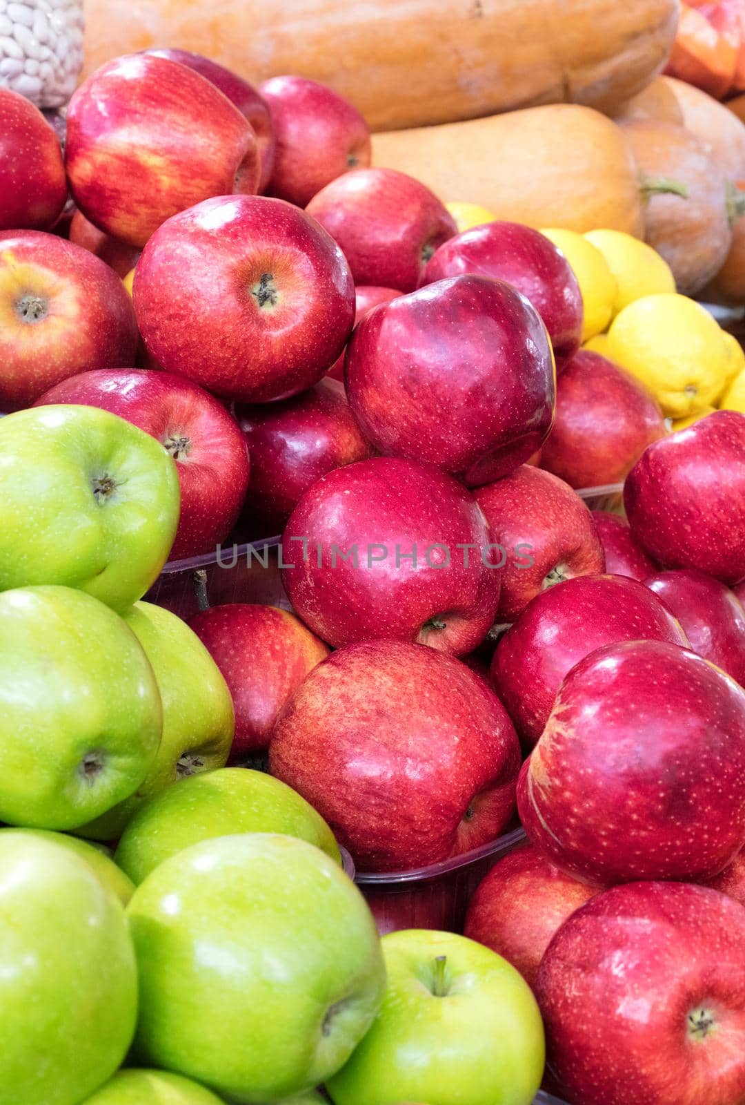 Bright picture of fresh red and green apples, lemons, pumpkins and other vegetables for sale in the market. Vertical image, close-up.