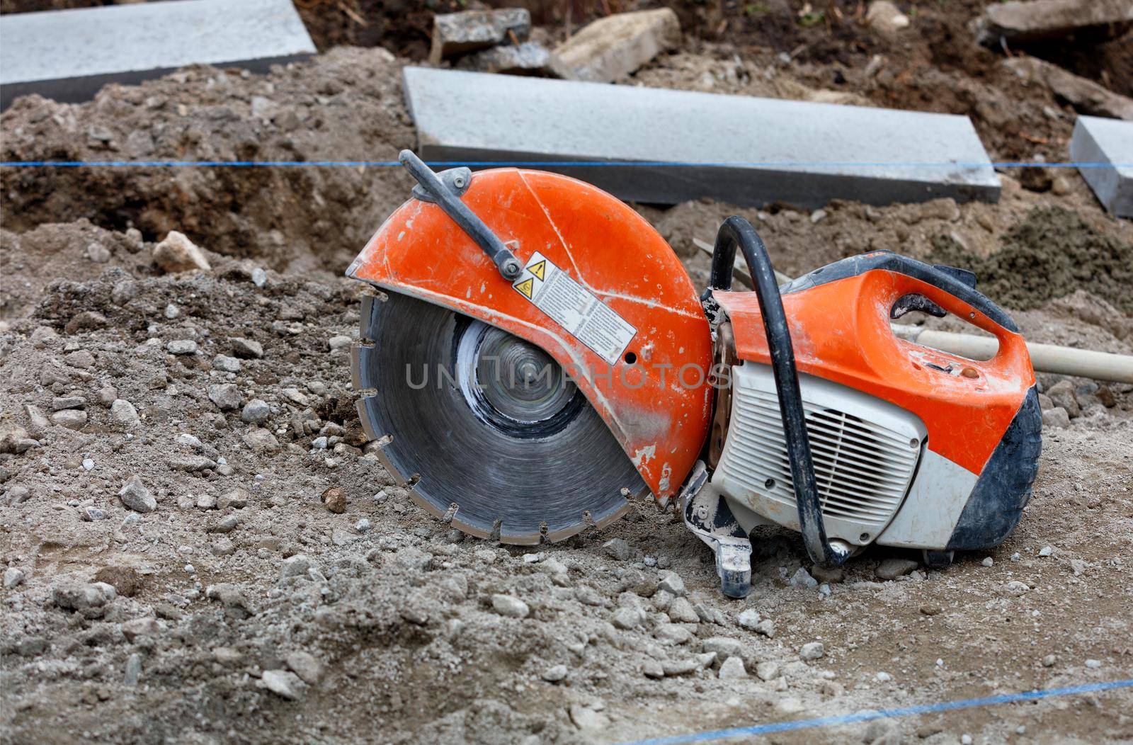 Petrol saw with diamond wheel on construction site gravel in front of concrete parapets. by Sergii