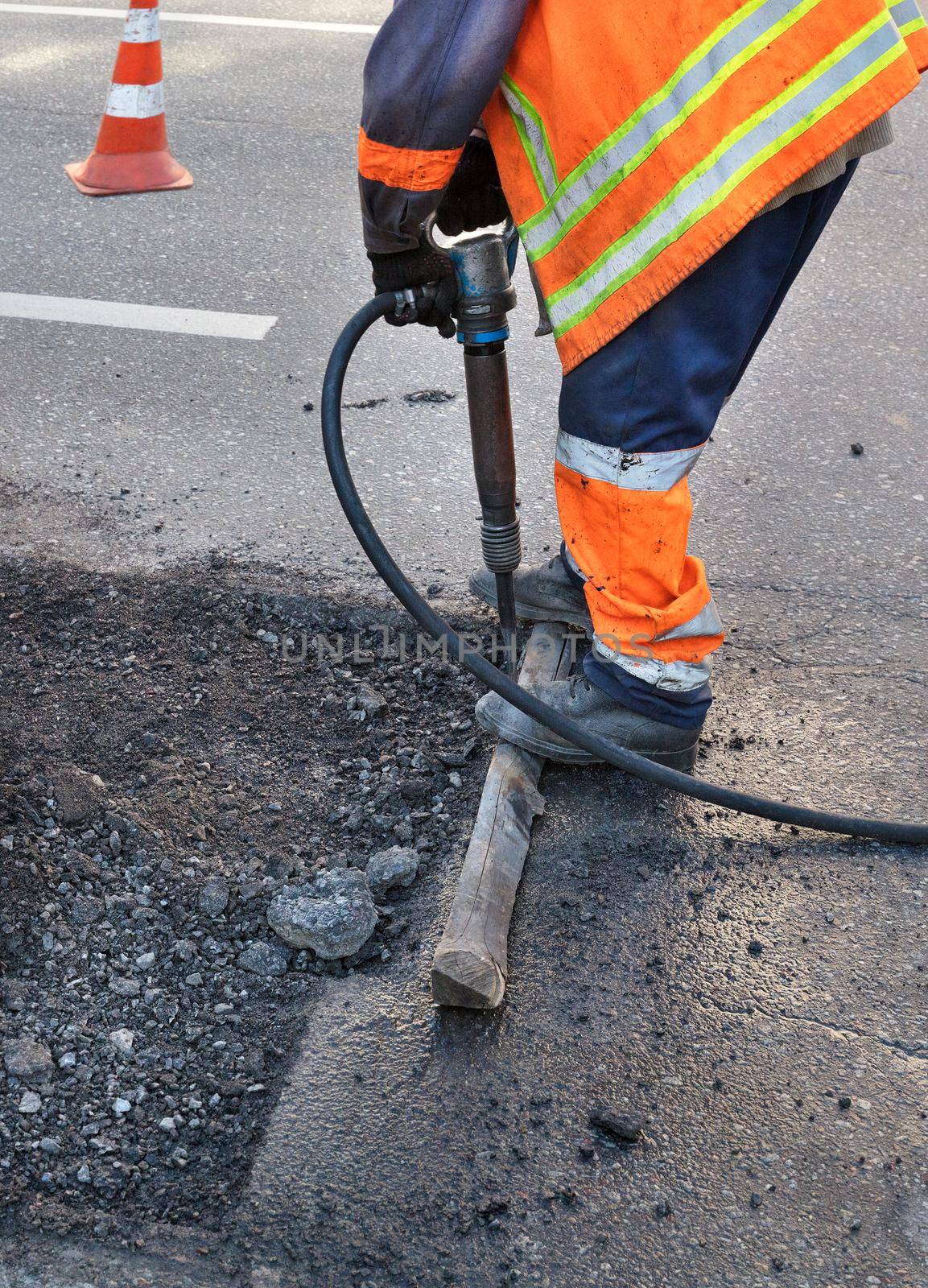 A road worker clears some of the asphalt with a jackhammer while repairing a road. by Sergii