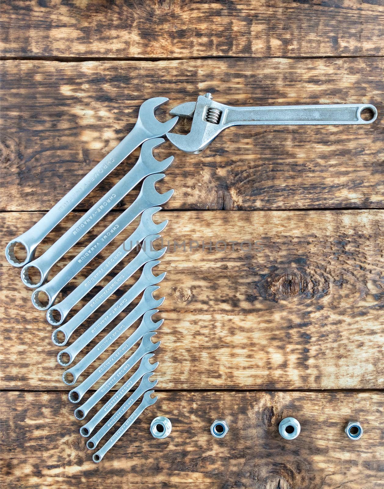 A set of wrenches with chrome vanadium and an adjustable wrench on a background of old wooden boards. Copy space, vertical image, close-up.