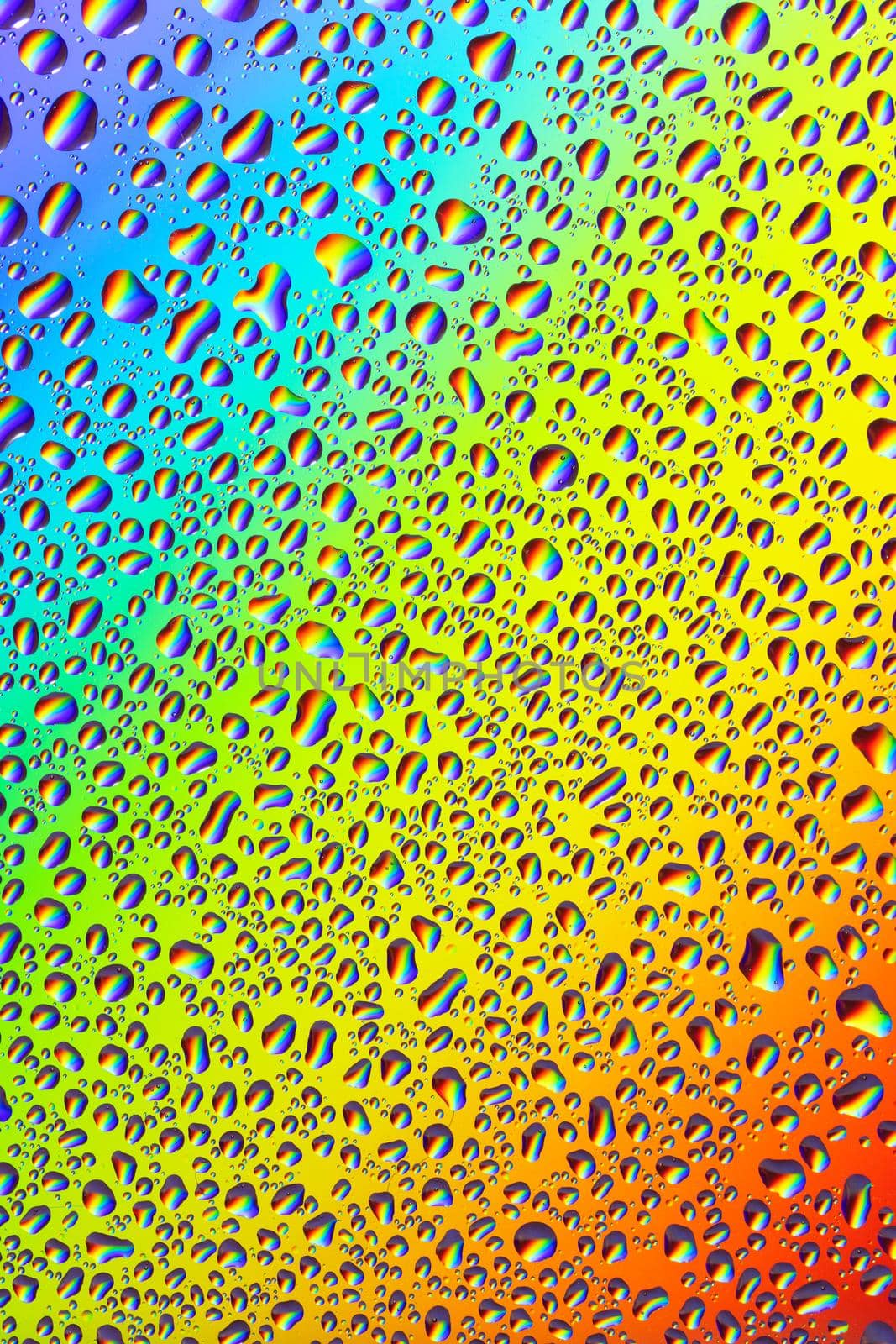 Water drops on a bright rainbow background and the reflection of the rainbow in them, close-up, high resolution, vertical image.