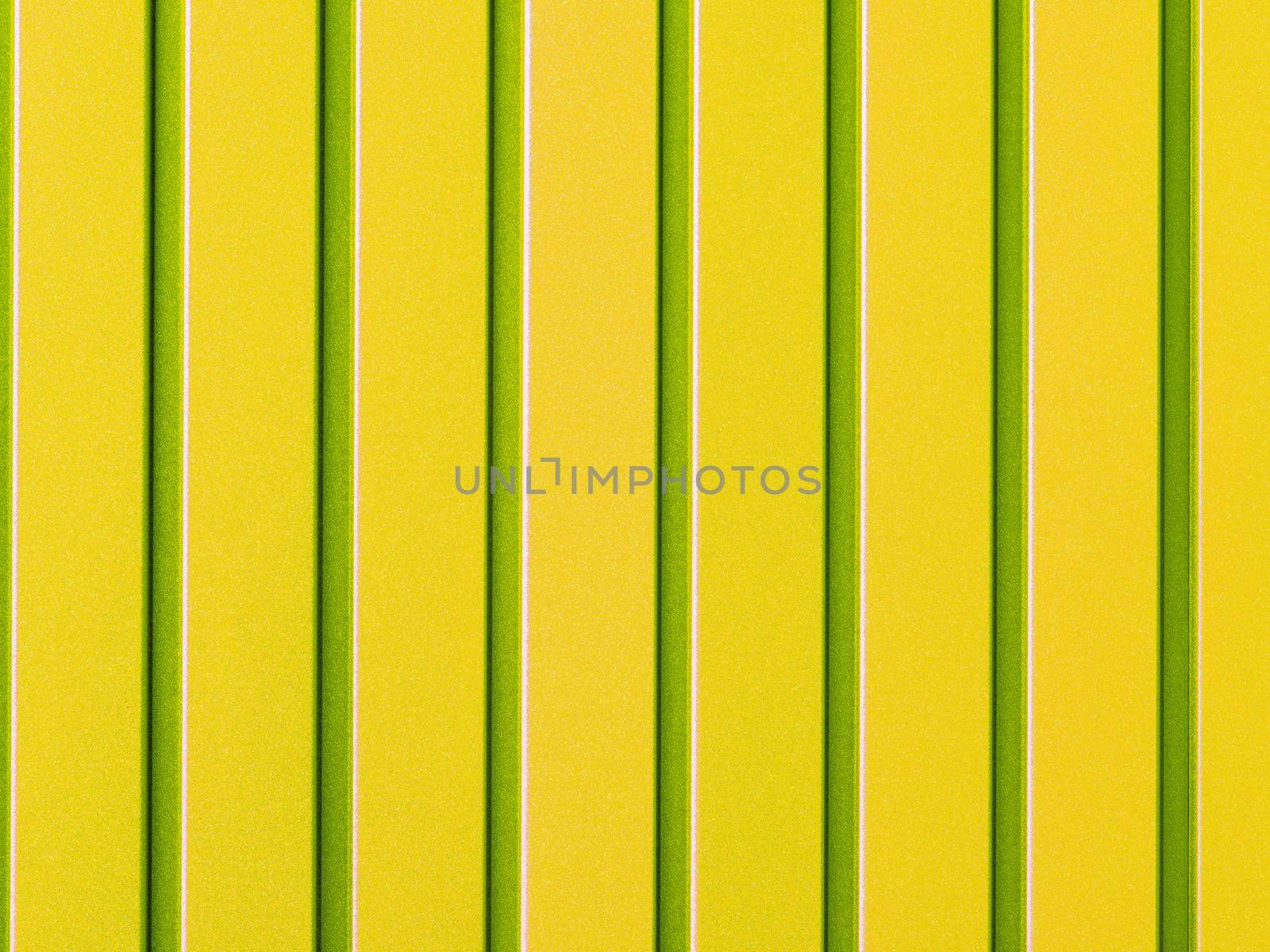 Yellow metal fence made of corrugated steel sheet with vertical rails. Corrugated yellow with light green stripes iron sheet close up background.