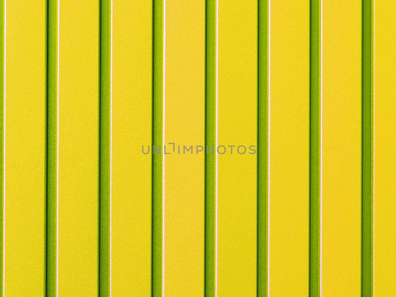 Yellow metal fence made of corrugated steel sheet with vertical rails. Corrugated yellow with light green stripes iron sheet close up background.