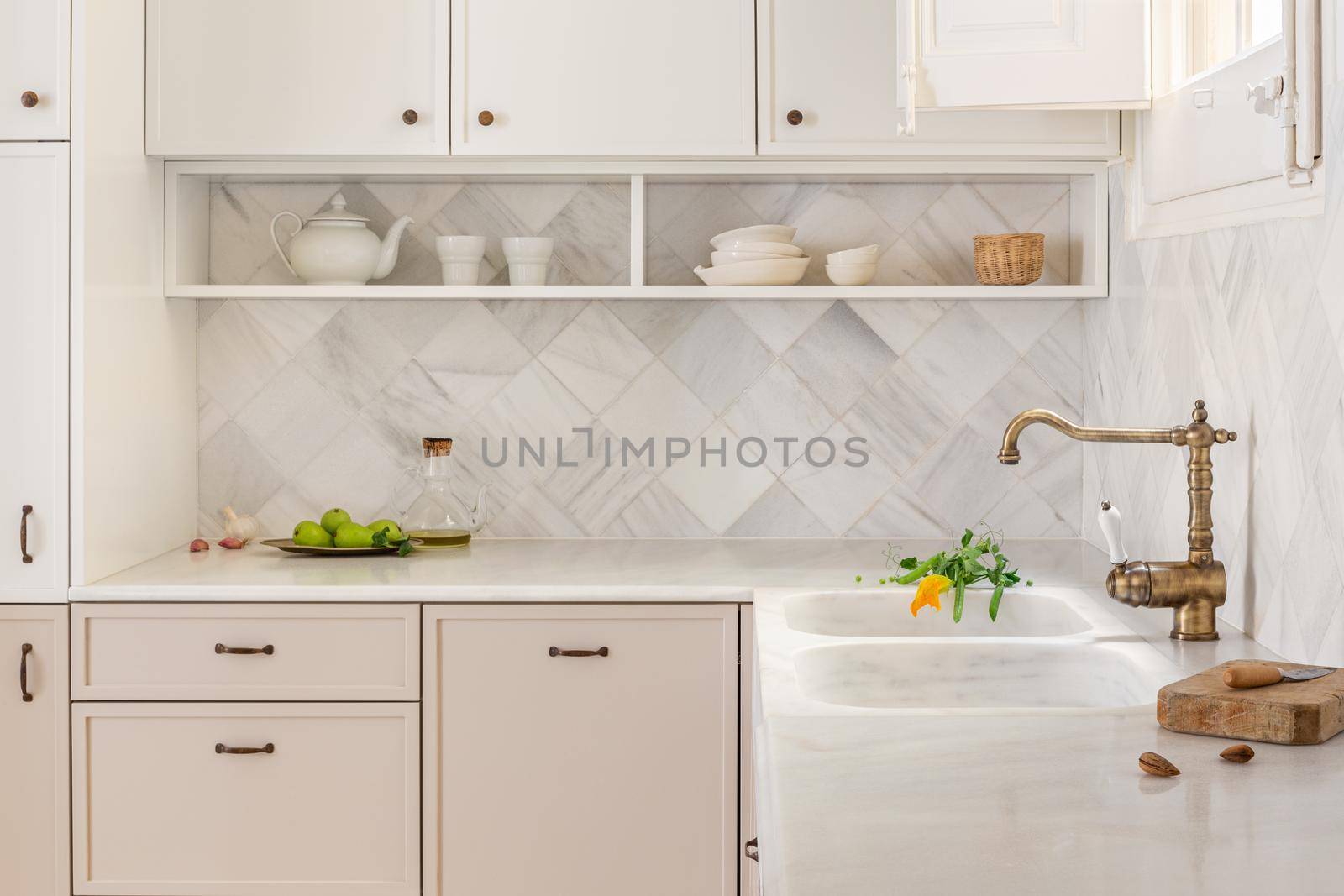 Kitchen interior with light furniture in rustic and retro style with tiled marble walls and vintage faucet. Fresh fruits on the table top. Natural light