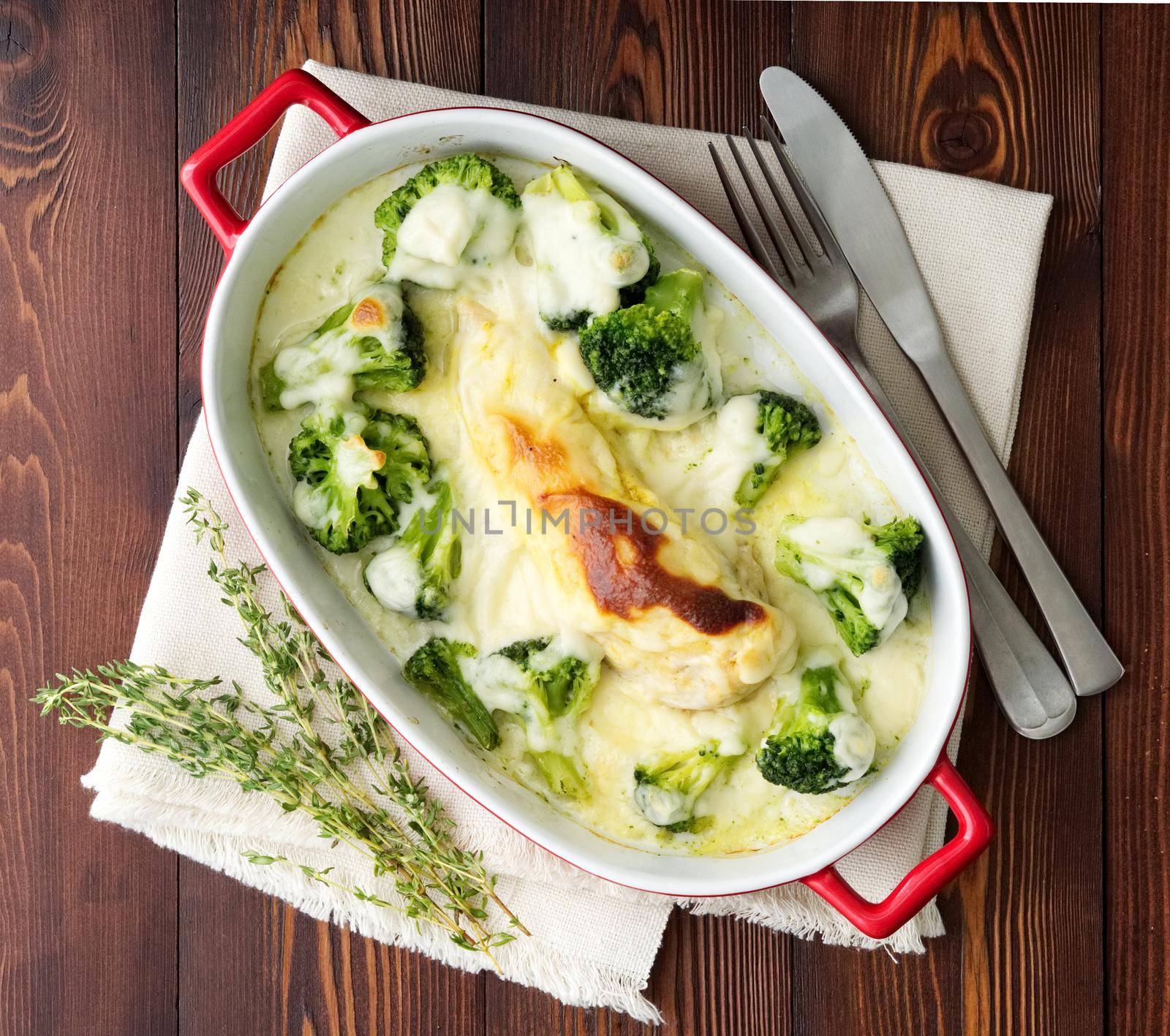 Chicken fillet baked with broccoli in bechamel sauce on dark wooden table. Healthy food by NataBene