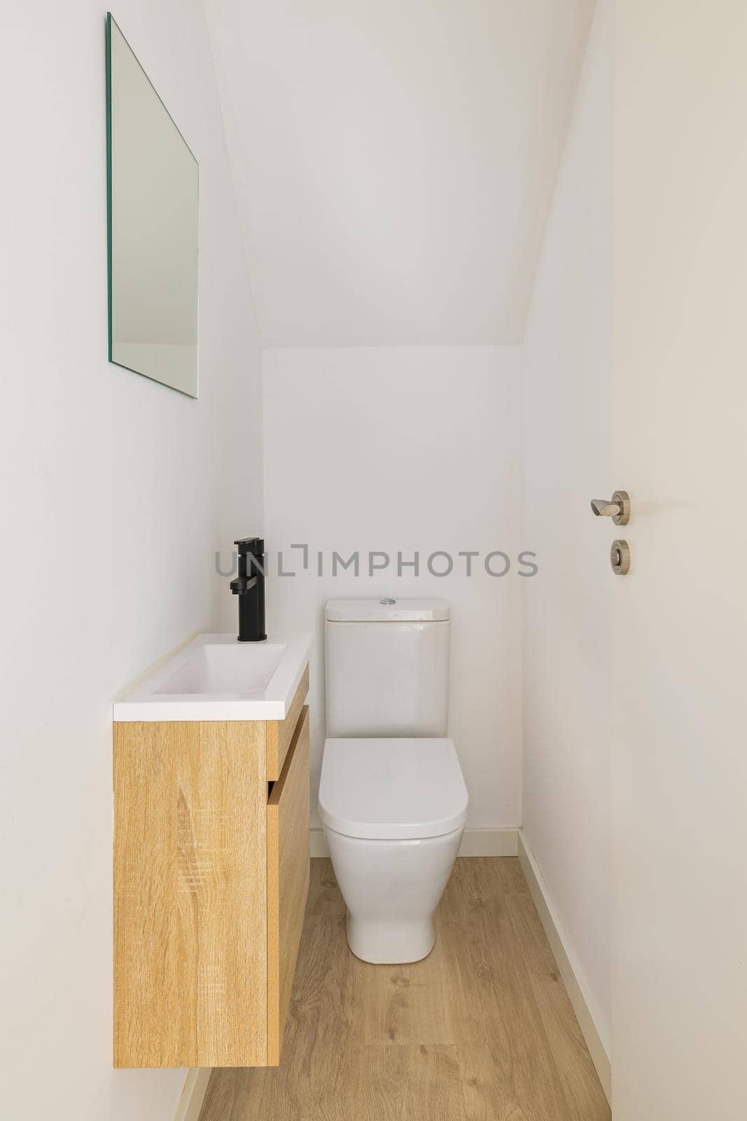 Narrow white toilet with small sink, mirror and wooden furniture