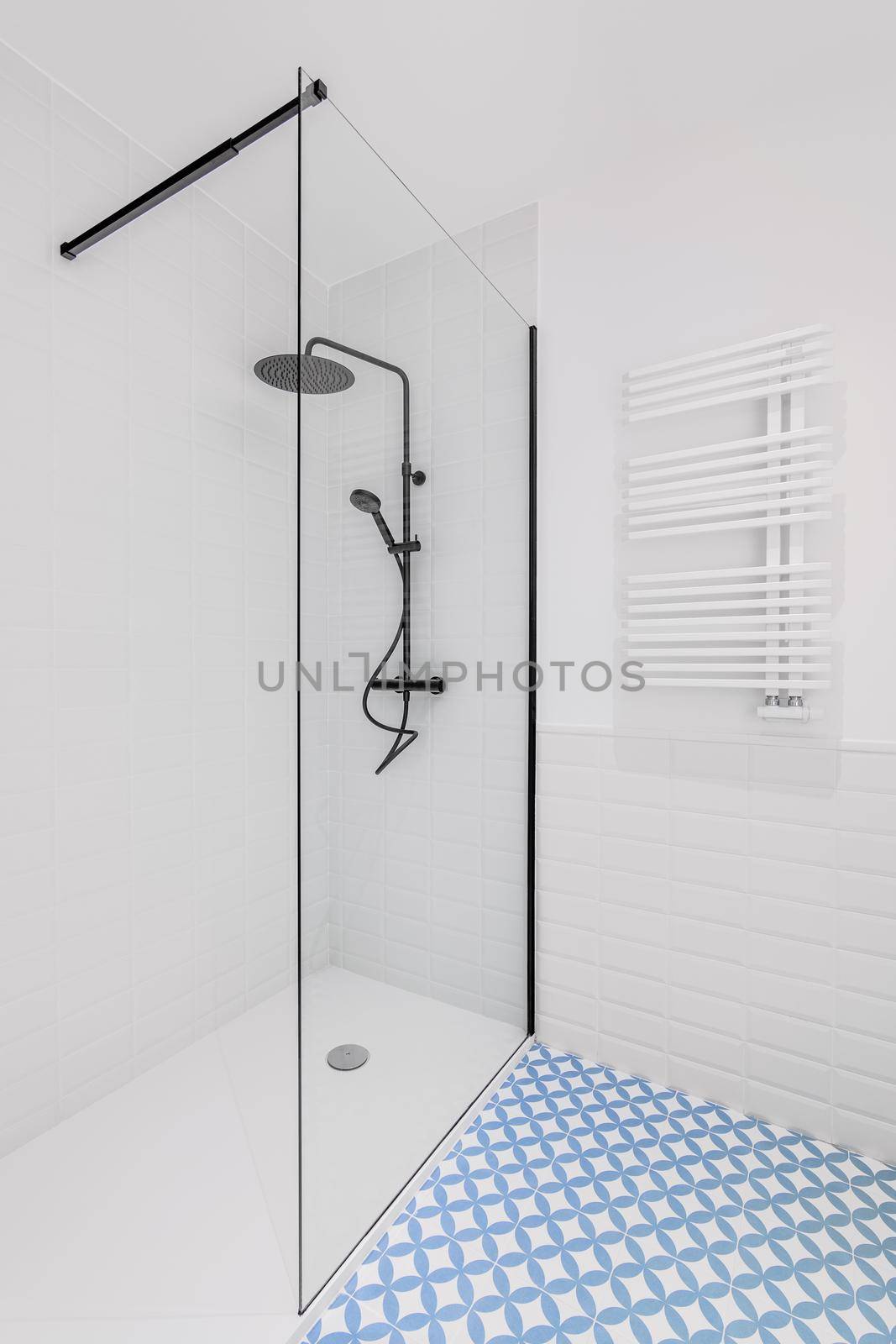 Bathroom decorated with light blue and white tiles. Modern shower zone with big rain head, hand held shower and glass door