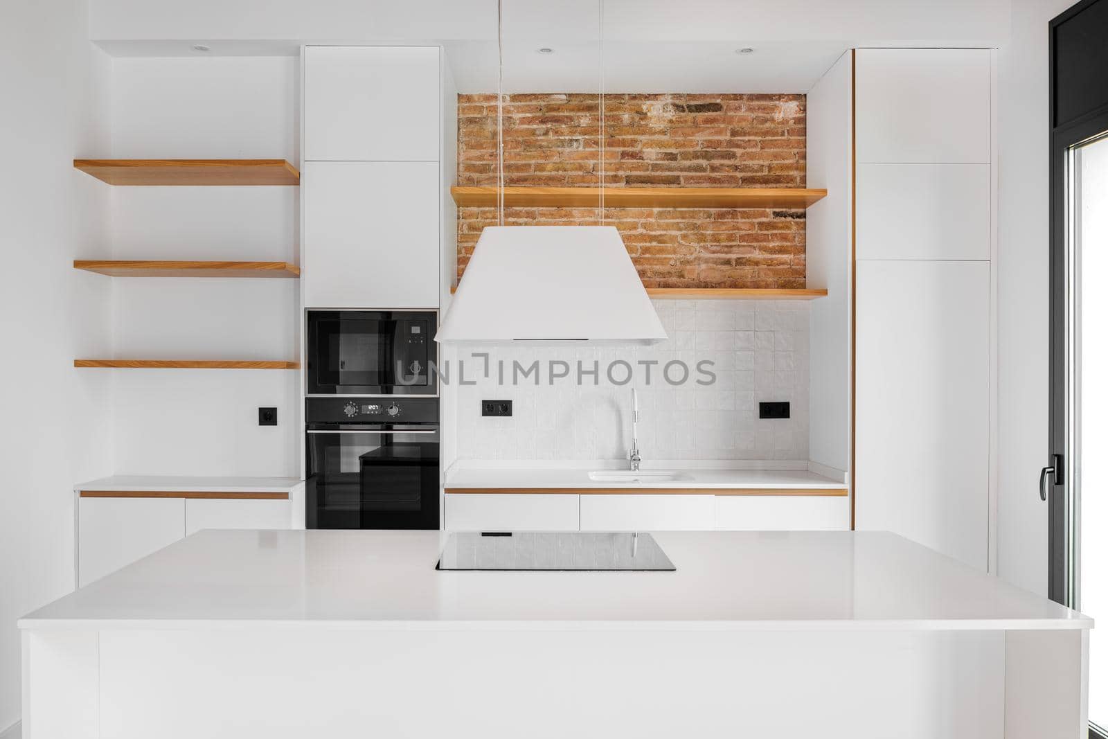 Modern furnished loft apartment with white island kitchen, big countertop, wooden shelves and brick wall.